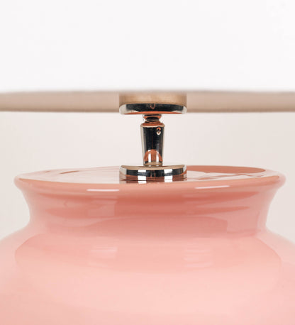 Candeeiro de mesa com um design rústico e sofisticado. A base do candeeiro é de barro vidrado de tom rosa salmão. A forma da base é arredondada com uma borda superior mais estreita, lembrando um vaso tradicional. A superfície da base é decorada com um padrão de relevos ovais. O suporte da lâmpada é em níquel polido e é manipulável. O cabo é revestido têxtil com um padrão trançado de tom rosa velho, com interruptor e ficha transparentes. O abatjour é cónico, em algodão, de tom bege claro.