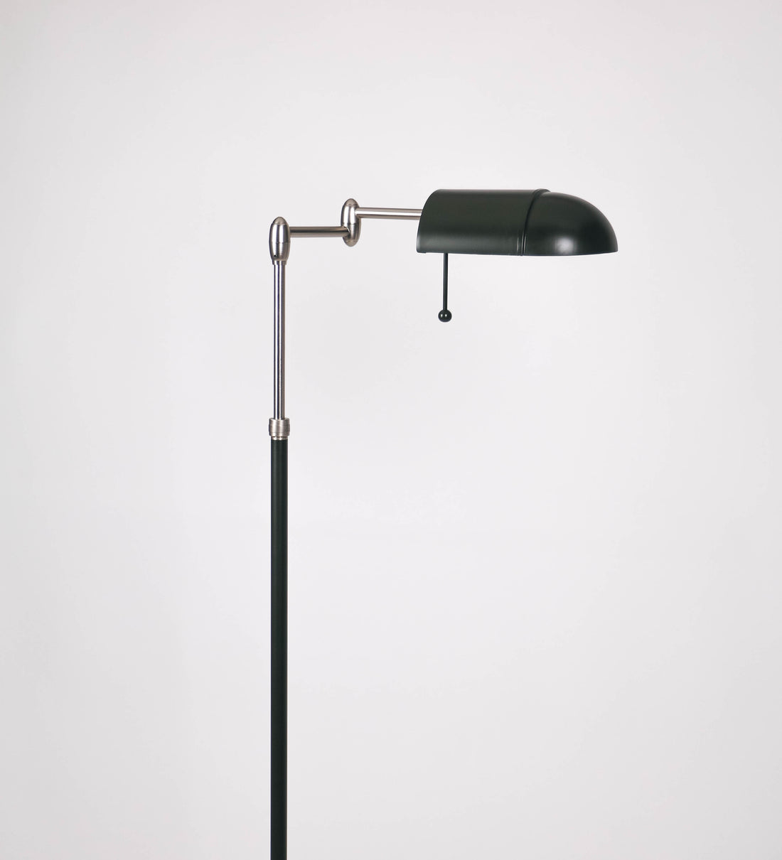Candeeiro de pé com base circular em verde-azeitona. O corpo é fino e vertical, composto por uma haste verde-azeitona, e uma outra haste em níquel escovado, que permite ajustar a altura do candeeiro. A haste ajustável conecta a um braço horizontal, que sustenta o chapéu, e é manipulável. O chapéu é longo e arredondado, em verde-azeitona, e com uma pequena haste com uma esfera na ponta. O interior do chapéu é branco. O cabo é revestido têxtil em preto, com um interruptor de pé preto circular.