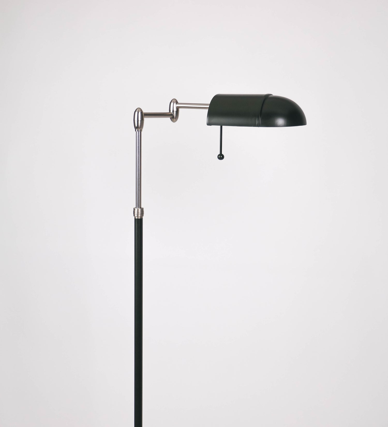 Candeeiro de pé com base circular em verde-azeitona. O corpo é fino e vertical, composto por uma haste verde-azeitona, e uma outra haste em níquel escovado, que permite ajustar a altura do candeeiro. A haste ajustável conecta a um braço horizontal, que sustenta o chapéu, e é manipulável. O chapéu é longo e arredondado, em verde-azeitona, e com uma pequena haste com uma esfera na ponta. O interior do chapéu é branco. O cabo é revestido têxtil em preto, com um interruptor de pé preto circular.