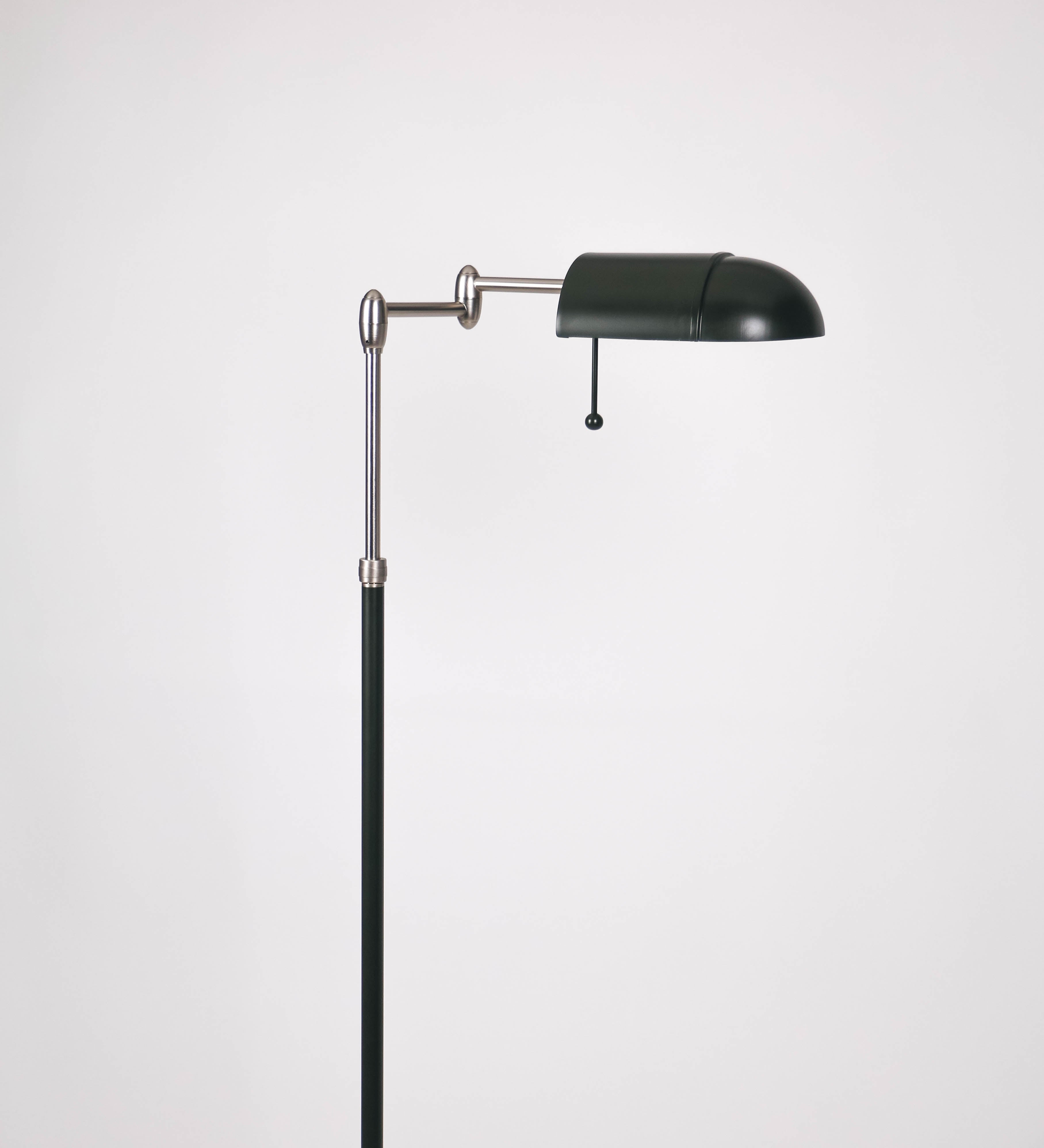 Candeeiro de pé com base circular em verde-azeitona. O corpo é fino e vertical, composto por uma haste verde-azeitona, e uma outra haste em níquel escovado, que permite ajustar a altura do candeeiro. A haste ajustável conecta a um braço horizontal, que sustenta o chapéu, e é manipulável. O chapéu é longo e arredondado, em verde-azeitona, e com uma pequena haste com uma esfera na ponta. O interior do chapéu é branco. O cabo é revestido têxtil em preto, com um interruptor de pé preto circular.