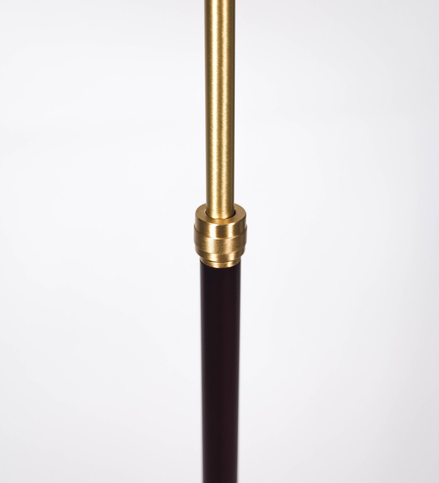 Candeeiro de pé com base circular em tom vinho. O corpo é fino e vertical, composto por uma haste tom vinho, e uma outra haste em latão escovado, que permite ajustar a altura do candeeiro. A haste ajustável conecta a um braço horizontal, que sustenta o chapéu, e é manipulável. O chapéu é longo e arredondado, em tom vinho, e com uma pequena haste com uma esfera na ponta. O interior do chapéu é branco. O cabo é revestido têxtil em preto, com um interruptor de pé preto circular.