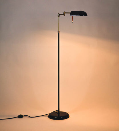 Candeeiro de pé com base circular em tom vinho. O corpo é fino e vertical, composto por uma haste tom vinho, e uma outra haste em latão escovado, que permite ajustar a altura do candeeiro. A haste ajustável conecta a um braço horizontal, que sustenta o chapéu, e é manipulável. O chapéu é longo e arredondado, em tom vinho, e com uma pequena haste com uma esfera na ponta. O interior do chapéu é branco. O cabo é revestido têxtil em preto, com um interruptor de pé preto circular.