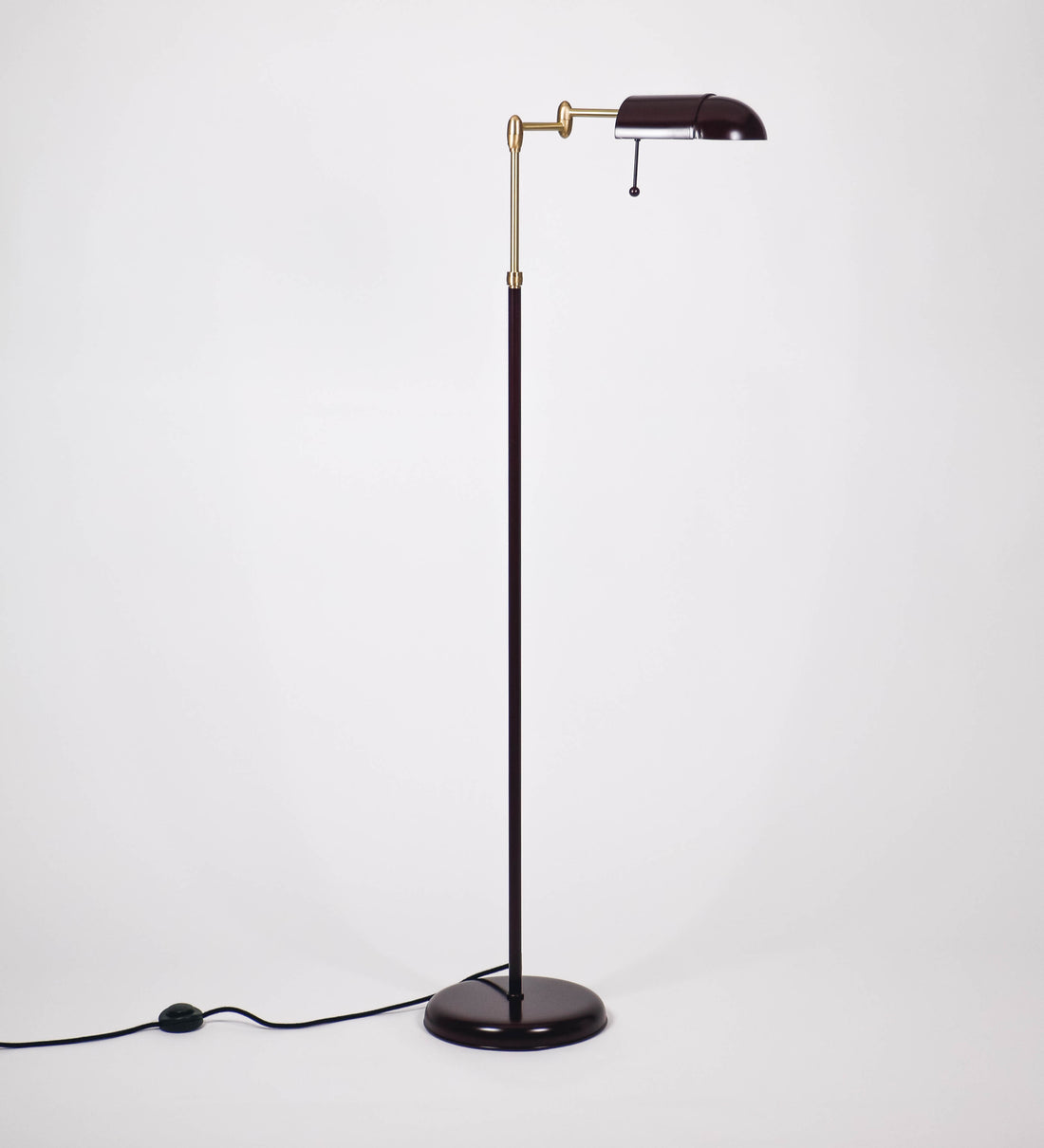 Candeeiro de pé com base circular em tom vinho. O corpo é fino e vertical, composto por uma haste tom vinho, e uma outra haste em latão escovado, que permite ajustar a altura do candeeiro. A haste ajustável conecta a um braço horizontal, que sustenta o chapéu, e é manipulável. O chapéu é longo e arredondado, em tom vinho, e com uma pequena haste com uma esfera na ponta. O interior do chapéu é branco. O cabo é revestido têxtil em preto, com um interruptor de pé preto circular.