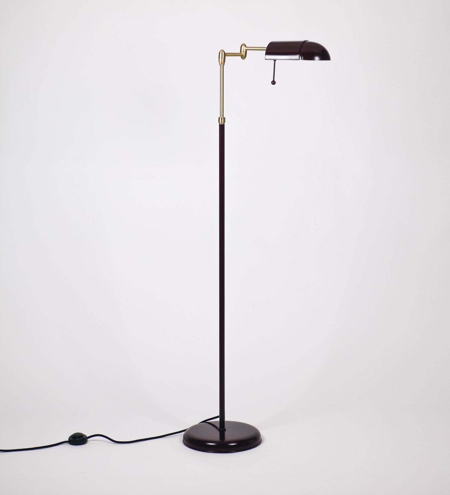 Candeeiro de pé com base circular em tom vinho. O corpo é fino e vertical, composto por uma haste tom vinho, e uma outra haste em latão escovado, que permite ajustar a altura do candeeiro. A haste ajustável conecta a um braço horizontal, que sustenta o chapéu, e é manipulável. O chapéu é longo e arredondado, em tom vinho, e com uma pequena haste com uma esfera na ponta. O interior do chapéu é branco. O cabo é revestido têxtil em preto, com um interruptor de pé preto circular.