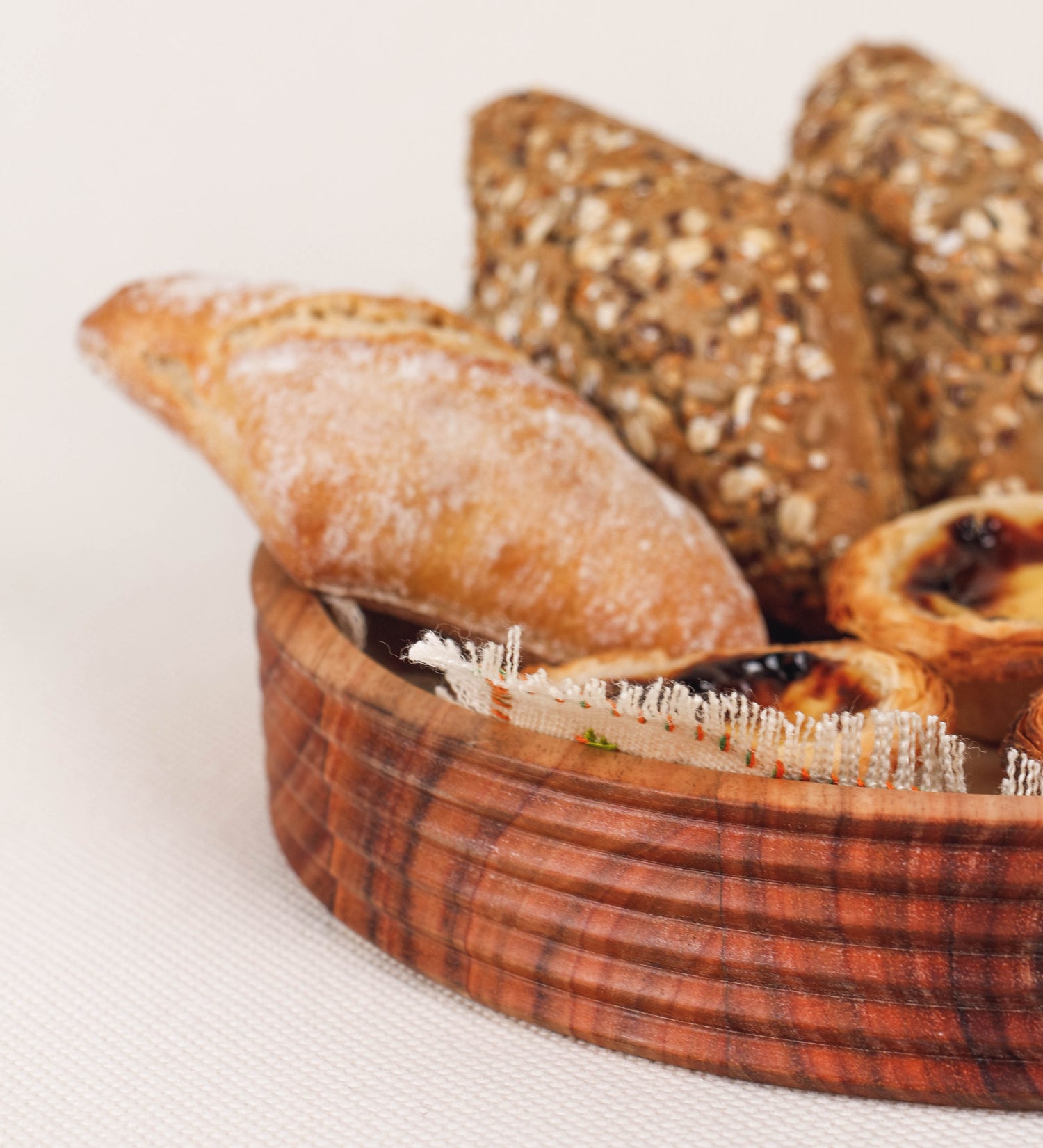 Fruteira com um design minimalista e distinto. A fruteira é de madeira de Acácia-Austrália, com uma tonalidade escura e verniz foodsafe semi-brilhante. A peça é de formato circular e com uma borda de cerca de 3 cm de altura, decorada com relevos lineares dispostos horizontalmente, tipo ranhuras, que envolvem a fruteira.