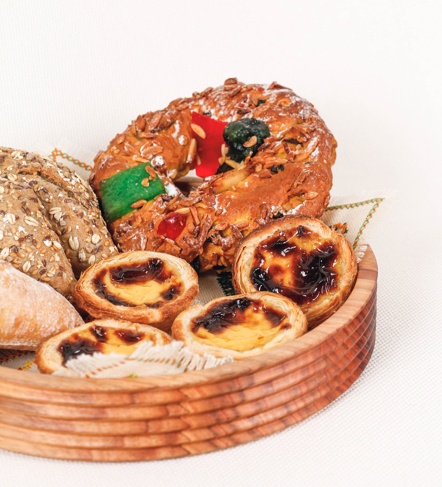 Fruteira com um design minimalista e distinto. A fruteira é de madeira de Acácia-Austrália, com uma tonalidade escura e verniz foodsafe semi-brilhante. A peça é de formato circular e com uma borda de cerca de 3 cm de altura, decorada com relevos lineares dispostos horizontalmente, tipo ranhuras, que envolvem a fruteira.