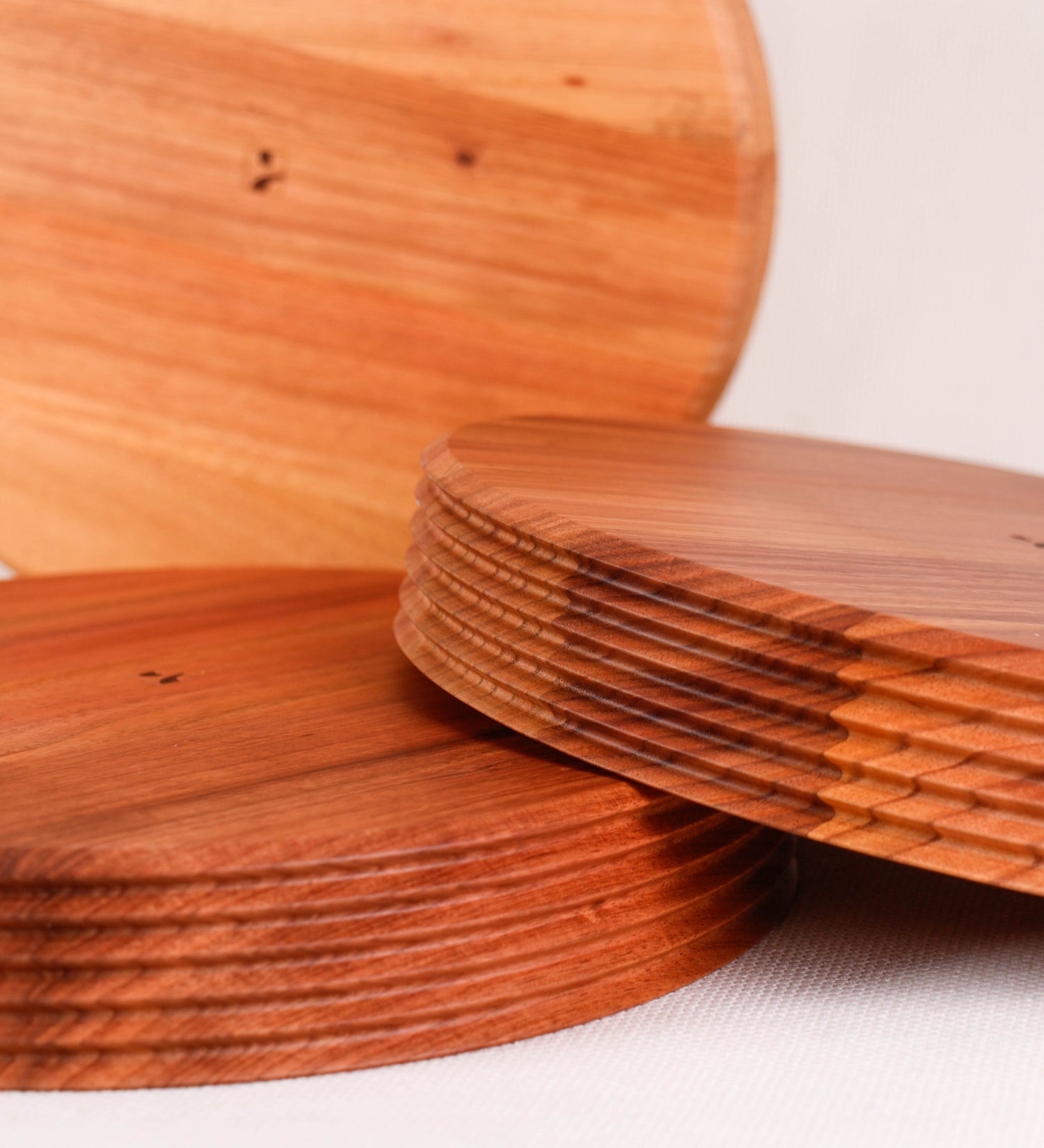 Fruteira com um design minimalista e distinto. A fruteira é de madeira de Acácia-Austrália, com uma tonalidade escura e verniz foodsafe semi-brilhante. A peça é de formato circular e com uma borda de cerca de 3 cm de altura, decorada com relevos lineares dispostos horizontalmente, tipo ranhuras, que envolvem a fruteira.