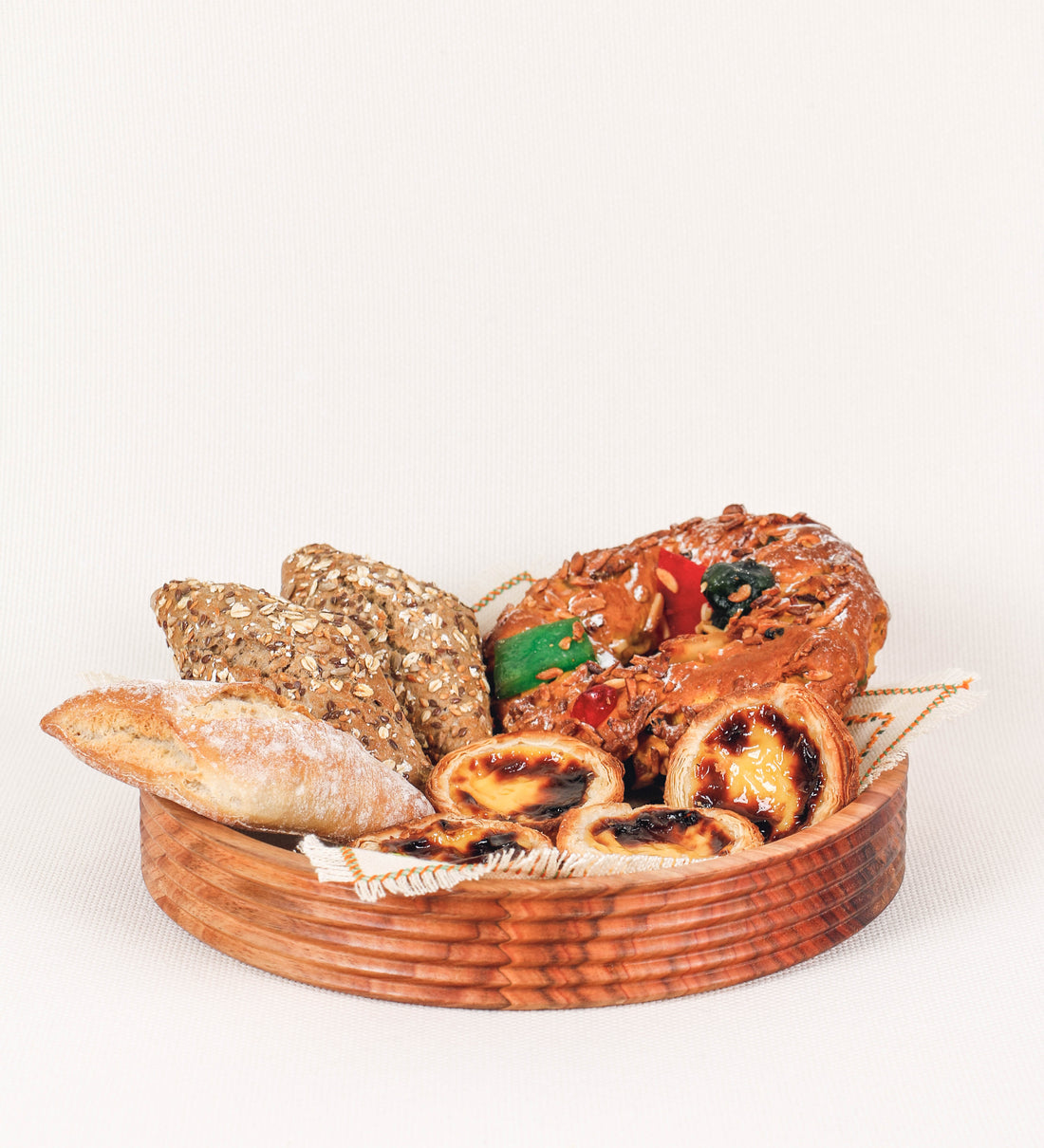 Fruteira com um design minimalista e distinto. A fruteira é de madeira de Acácia-Austrália, com uma tonalidade escura e verniz foodsafe semi-brilhante. A peça é de formato circular e com uma borda de cerca de 3 cm de altura, decorada com relevos lineares dispostos horizontalmente, tipo ranhuras, que envolvem a fruteira.