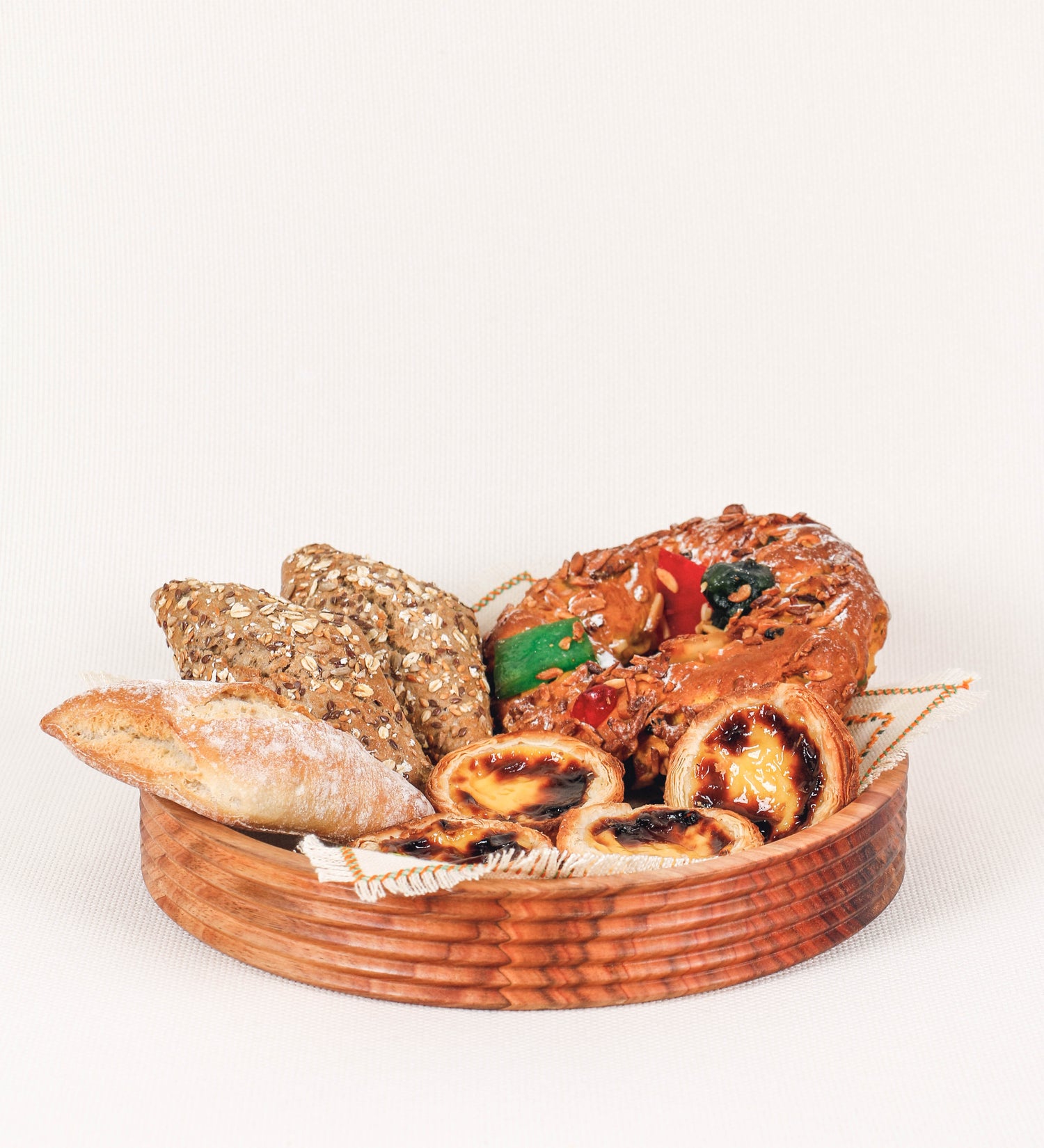 Fruteira com um design minimalista e distinto. A fruteira é de madeira de Acácia-Austrália, com uma tonalidade escura e verniz foodsafe semi-brilhante. A peça é de formato circular e com uma borda de cerca de 3 cm de altura, decorada com relevos lineares dispostos horizontalmente, tipo ranhuras, que envolvem a fruteira.