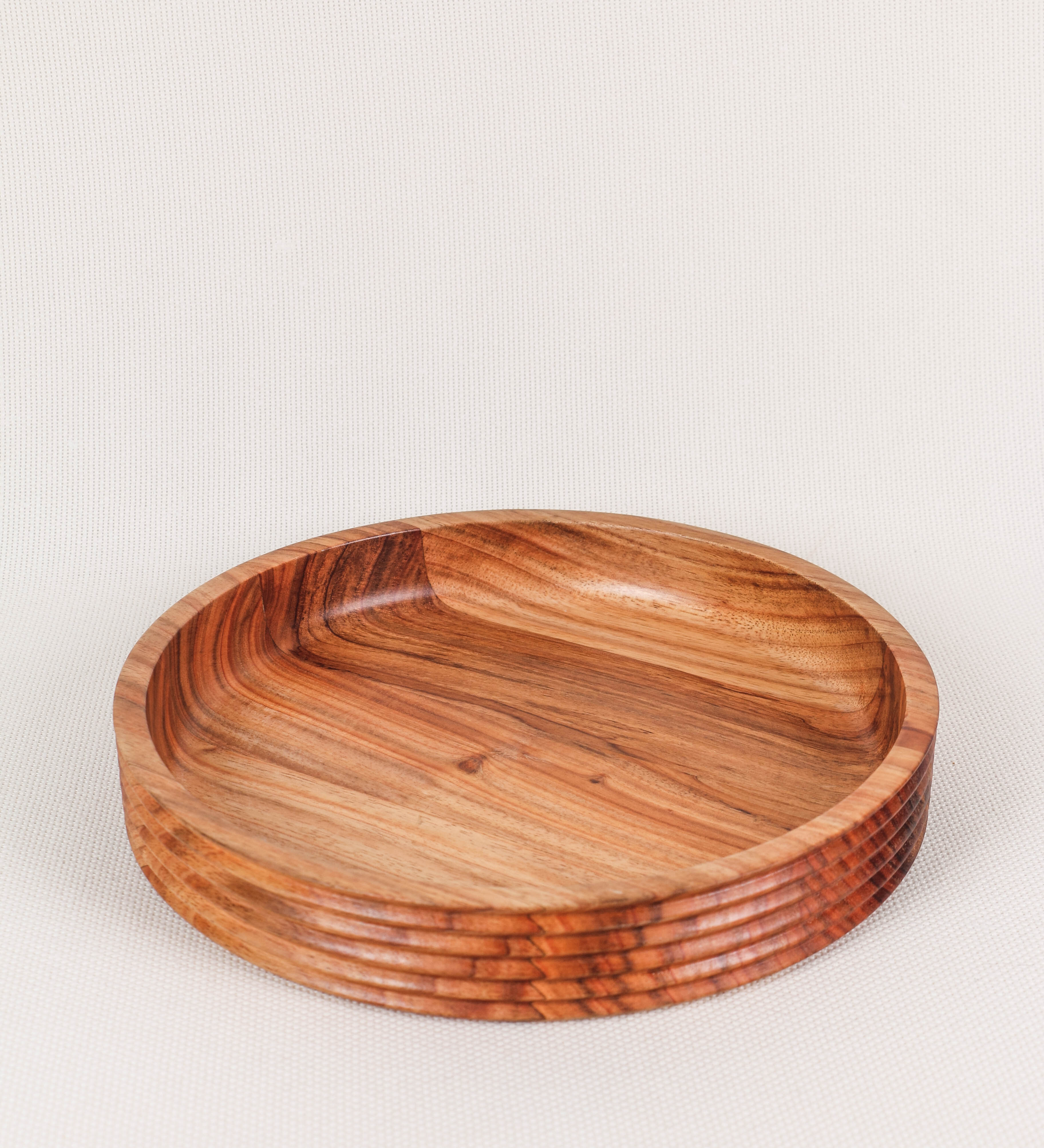 Fruteira com um design minimalista e distinto. A fruteira é de madeira de Acácia-Austrália, com uma tonalidade escura e verniz foodsafe semi-brilhante. A peça é de formato circular e com uma borda de cerca de 3 cm de altura, decorada com relevos lineares dispostos horizontalmente, tipo ranhuras, que envolvem a fruteira.