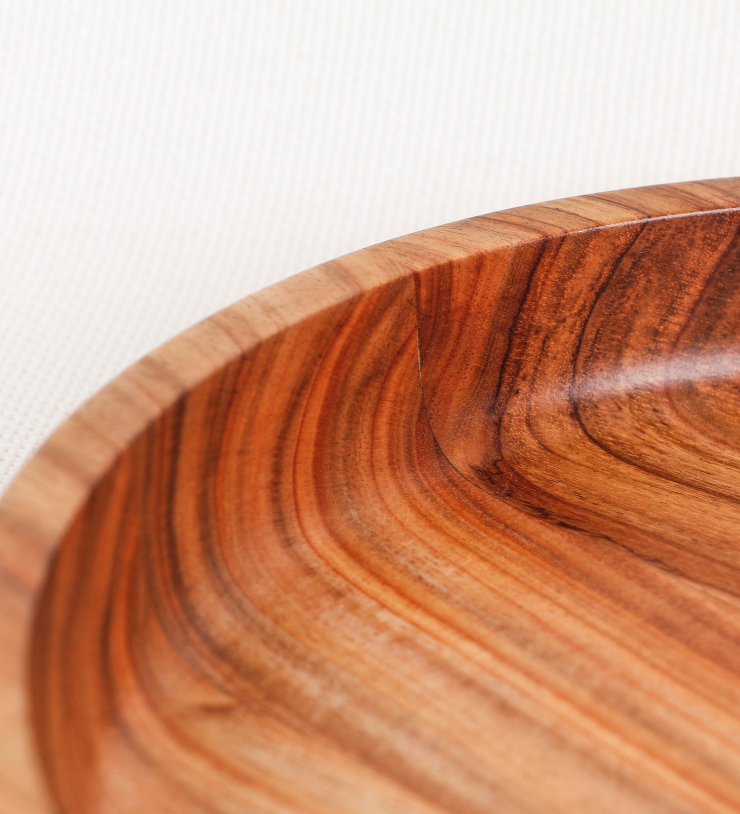 Fruteira com um design minimalista e distinto. A fruteira é de madeira de Acácia-Austrália, com uma tonalidade escura e verniz foodsafe semi-brilhante. A peça é de formato circular e com uma borda de cerca de 3 cm de altura, decorada com relevos lineares dispostos horizontalmente, tipo ranhuras, que envolvem a fruteira.