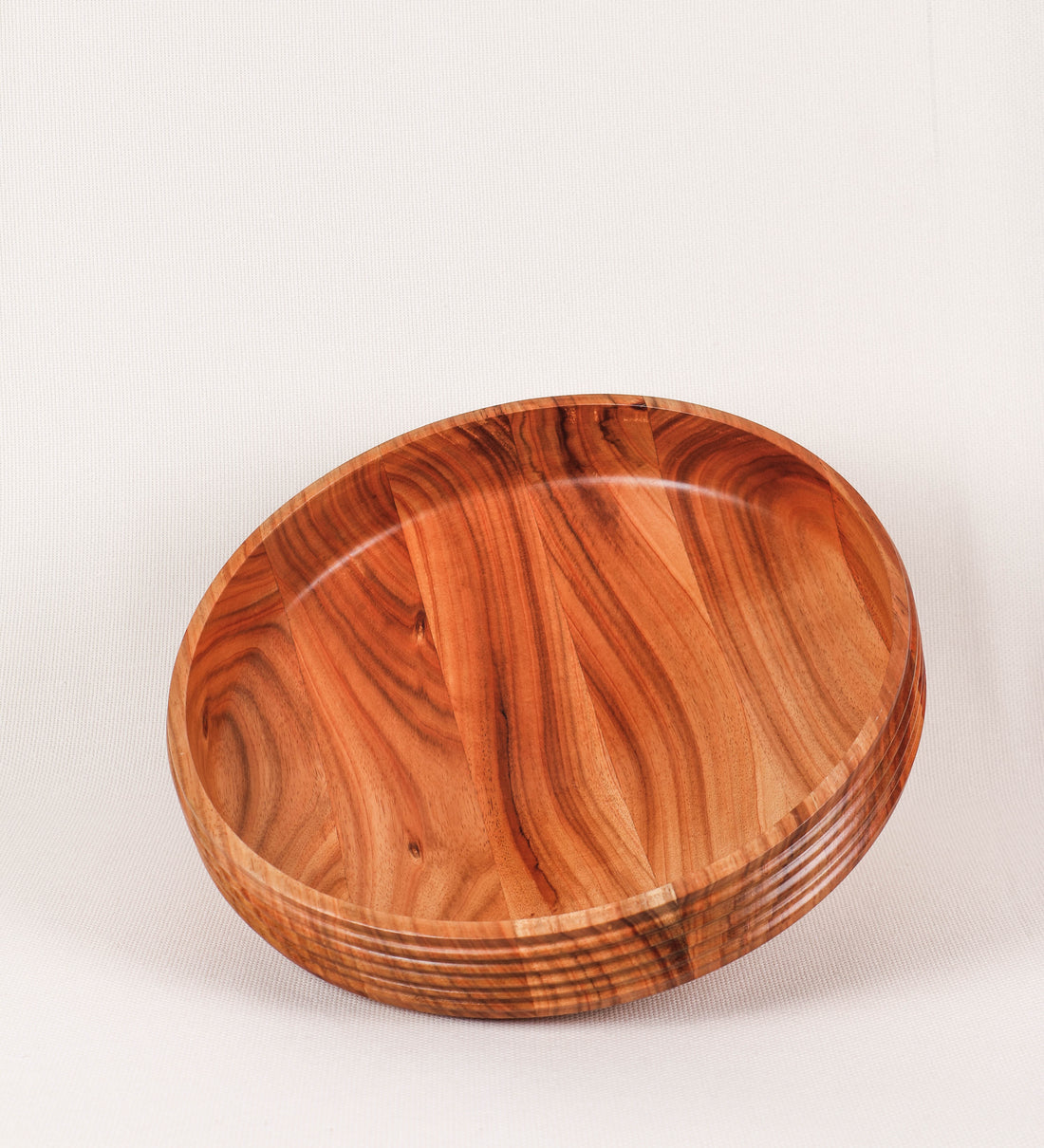 Fruteira com um design minimalista e distinto. A fruteira é de madeira de Acácia-Austrália, com uma tonalidade escura e verniz foodsafe semi-brilhante. A peça é de formato cónico e com um toque liso, semelhante a um pião, com uma ponteira em madeira também de tom mais escuro, quase negro. Apresenta ainda uma borda de cerca de 3 cm de altura, próxima da abertura da peça, decorada com relevos lineares dispostos horizontalmente, tipo ranhuras, que envolvem a fruteira.