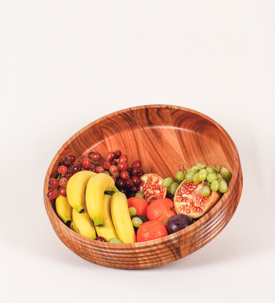 Fruteira com um design minimalista e distinto. A fruteira é de madeira de Acácia-Austrália, com uma tonalidade escura e verniz foodsafe semi-brilhante. A peça é de formato cónico e com um toque liso, semelhante a um pião, com uma ponteira em madeira também de tom mais escuro, quase negro. Apresenta ainda uma borda de cerca de 3 cm de altura, próxima da abertura da peça, decorada com relevos lineares dispostos horizontalmente, tipo ranhuras, que envolvem a fruteira.