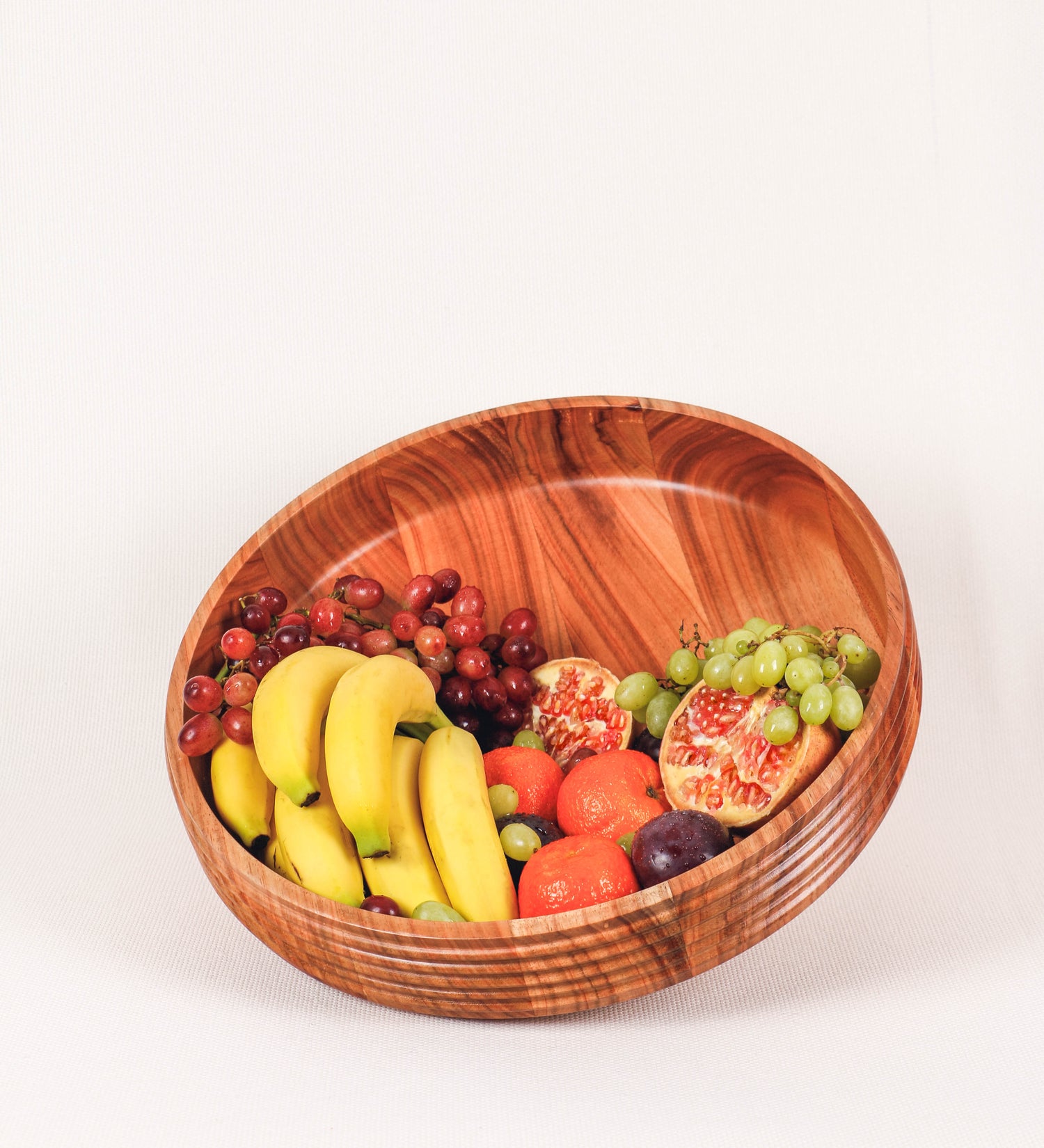 Fruteira com um design minimalista e distinto. A fruteira é de madeira de Acácia-Austrália, com uma tonalidade escura e verniz foodsafe semi-brilhante. A peça é de formato cónico e com um toque liso, semelhante a um pião, com uma ponteira em madeira também de tom mais escuro, quase negro. Apresenta ainda uma borda de cerca de 3 cm de altura, próxima da abertura da peça, decorada com relevos lineares dispostos horizontalmente, tipo ranhuras, que envolvem a fruteira.