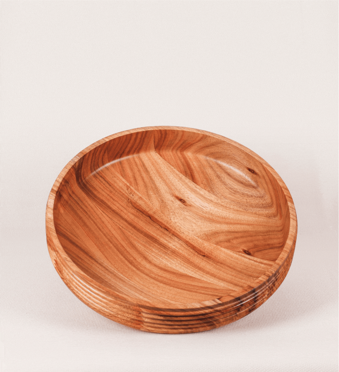 Fruteira com um design minimalista e distinto. A fruteira é de madeira de Acácia-Austrália, com uma tonalidade escura e verniz foodsafe semi-brilhante. A peça é de formato cónico e com um toque liso, semelhante a um pião, com uma ponteira em madeira também de tom mais escuro, quase negro. Apresenta ainda uma borda de cerca de 3 cm de altura, próxima da abertura da peça, decorada com relevos lineares dispostos horizontalmente, tipo ranhuras, que envolvem a fruteira.