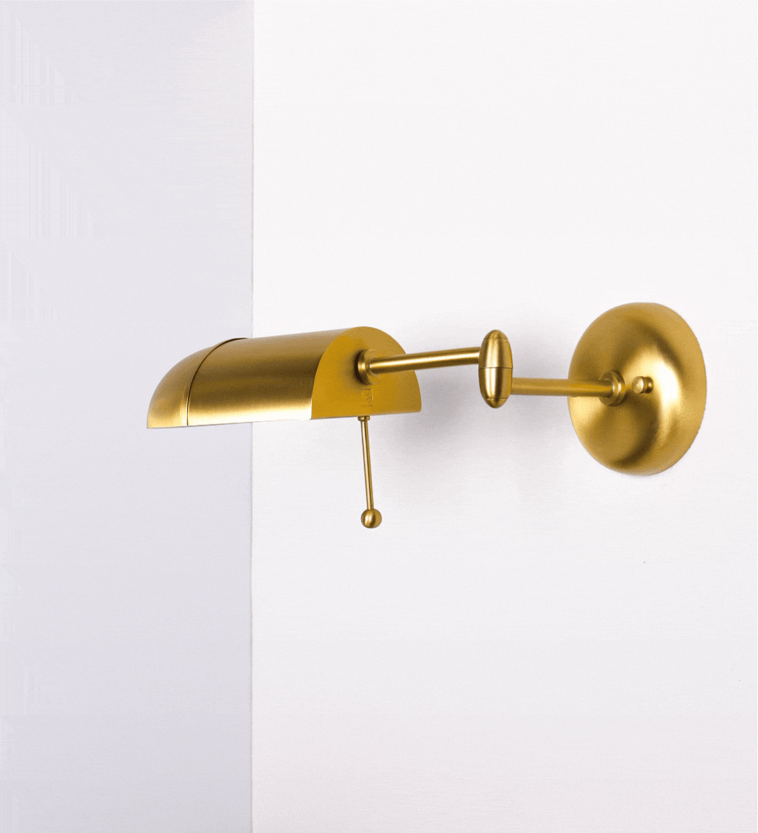 Aplique de parede com um design elegante e funcional. A base do aplique é redonda e fixa-se diretamente na parede. Do centro da sua base sai o braço do aplique, que é reto e horizontal. O braço é ajustável permitindo direcionar a luz. No final do braço, há um chapéu longo e arredondado e com uma pequena haste com uma esfera na ponta, que auxilia a movimentar o chapéu.