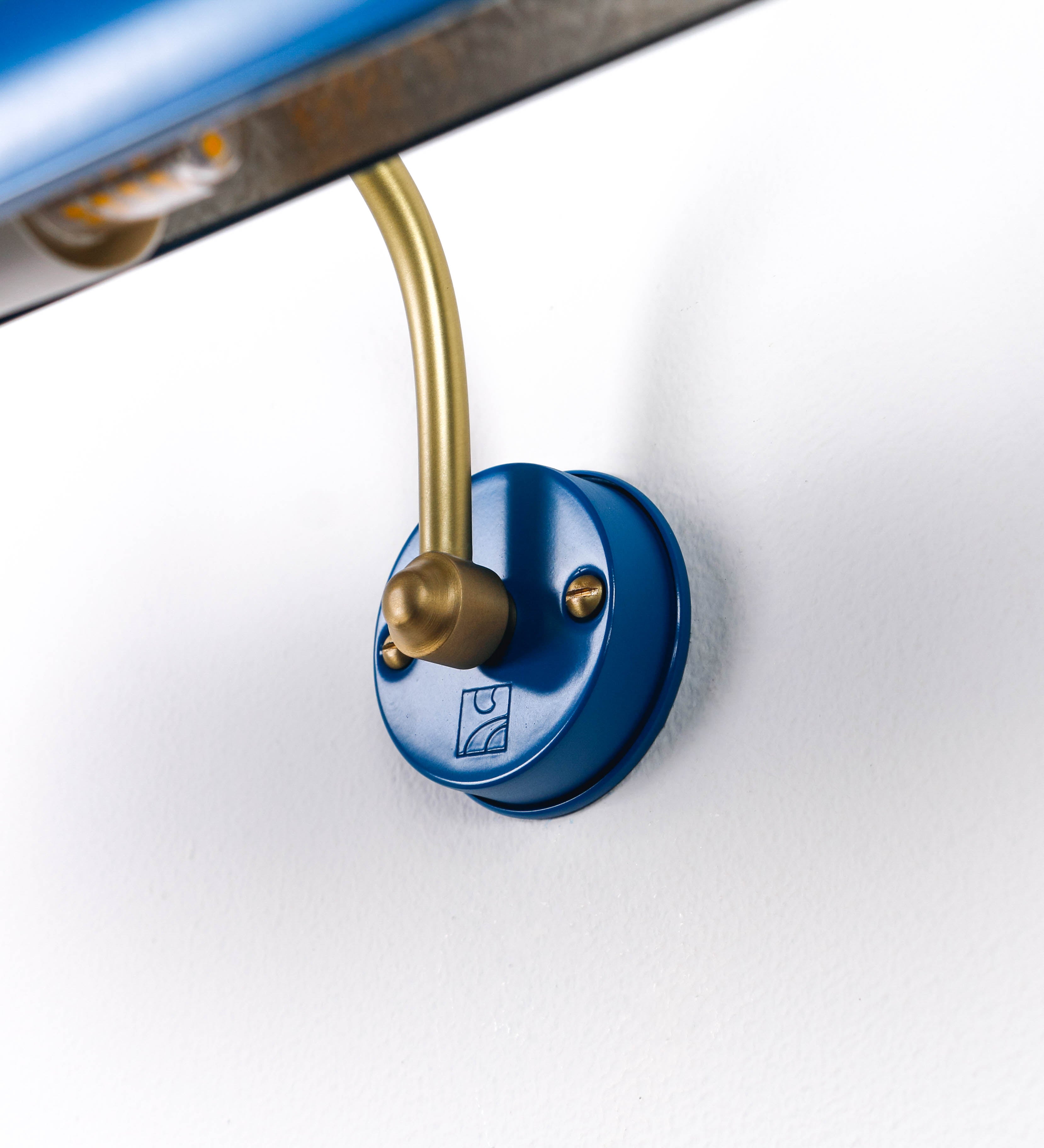 Aplique de parede que combina elementos clássicos com toques contemporâneos. O aplique é composto por uma base circular azul vintage de onde se estende um braço curvo e gracioso, em latão escovado, que suporta a barra principal. O braço contém um elemento, em latão escovado, que permite apertar ou desapertar a barra para melhor manipular a direção da luz. A barra de 45cm de largura, é cilíndrica e alongada, azul vintage. As extremidades do cilindro são planas e do mesmo diâmetro.