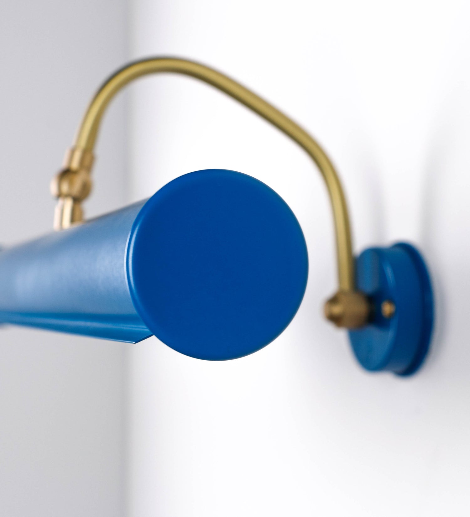 Aplique de parede que combina elementos clássicos com toques contemporâneos. O aplique é composto por uma base circular azul vintage de onde se estende um braço curvo e gracioso, em latão escovado, que suporta a barra principal. O braço contém um elemento, em latão escovado, que permite apertar ou desapertar a barra para melhor manipular a direção da luz. A barra de 45cm de largura, é cilíndrica e alongada, azul vintage. As extremidades do cilindro são planas e do mesmo diâmetro.