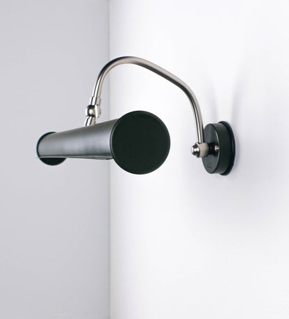 Aplique de parede que combina elementos clássicos com toques contemporâneos. O aplique é composto por uma base circular verde-azeitona, de onde se estende um braço curvo e gracioso, em níquel escovado, que suporta a barra principal. O braço contém um elemento, em níquel escovado, que permite apertar ou desapertar a barra para melhor manipular a direção da luz. A barra de 45cm de largura, é cilíndrica e alongada, verde-azeitona. As extremidades do cilindro são planas e do mesmo diâmetro.