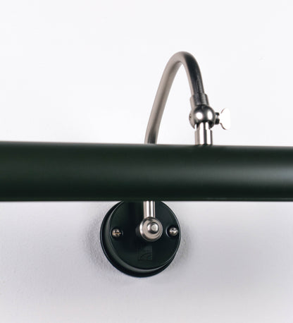 Aplique de parede que combina elementos clássicos com toques contemporâneos. O aplique é composto por uma base circular verde-azeitona, de onde se estende um braço curvo e gracioso, em níquel escovado, que suporta a barra principal. O braço contém um elemento, em níquel escovado, que permite apertar ou desapertar a barra para melhor manipular a direção da luz. A barra de 45cm de largura, é cilíndrica e alongada, verde-azeitona. As extremidades do cilindro são planas e do mesmo diâmetro.