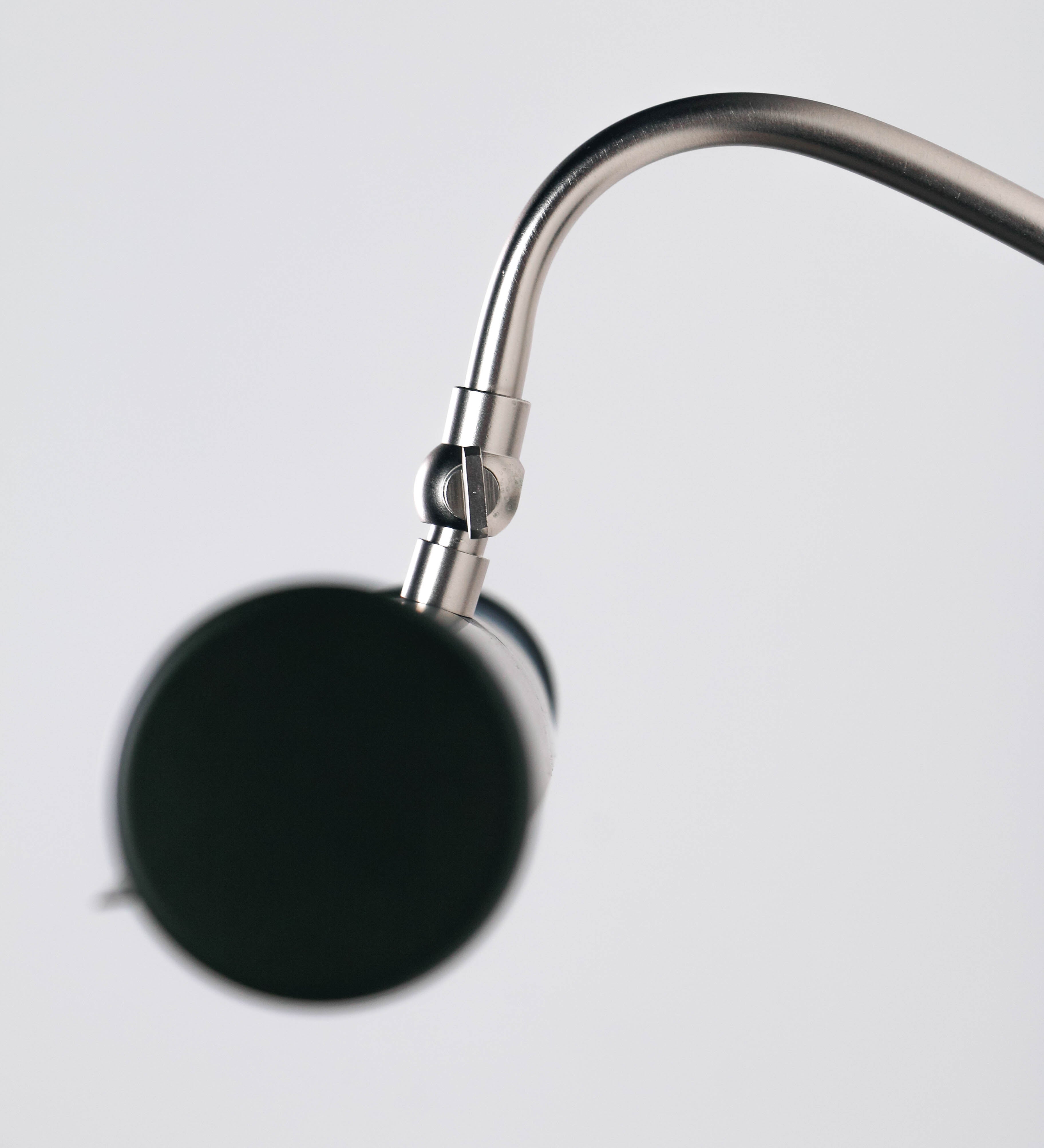 Aplique de parede que combina elementos clássicos com toques contemporâneos. O aplique é composto por uma base circular verde-azeitona, de onde se estende um braço curvo e gracioso, em níquel escovado, que suporta a barra principal. O braço contém um elemento, em níquel escovado, que permite apertar ou desapertar a barra para melhor manipular a direção da luz. A barra de 45cm de largura, é cilíndrica e alongada, verde-azeitona. As extremidades do cilindro são planas e do mesmo diâmetro.