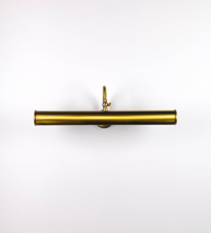 Aplique de parede que combina elementos clássicos com toques contemporâneos, todo em ouro velho. O aplique é composto por uma base circular de onde se estende um braço curvo e gracioso, que suporta a barra principal. O braço contém um elemento que permite apertar ou desapertar a barra para melhor manipular a direção da luz. A barra de 45cm de largura é cilíndrica e alongada. As extremidades do cilindro são planas e do mesmo diâmetro.