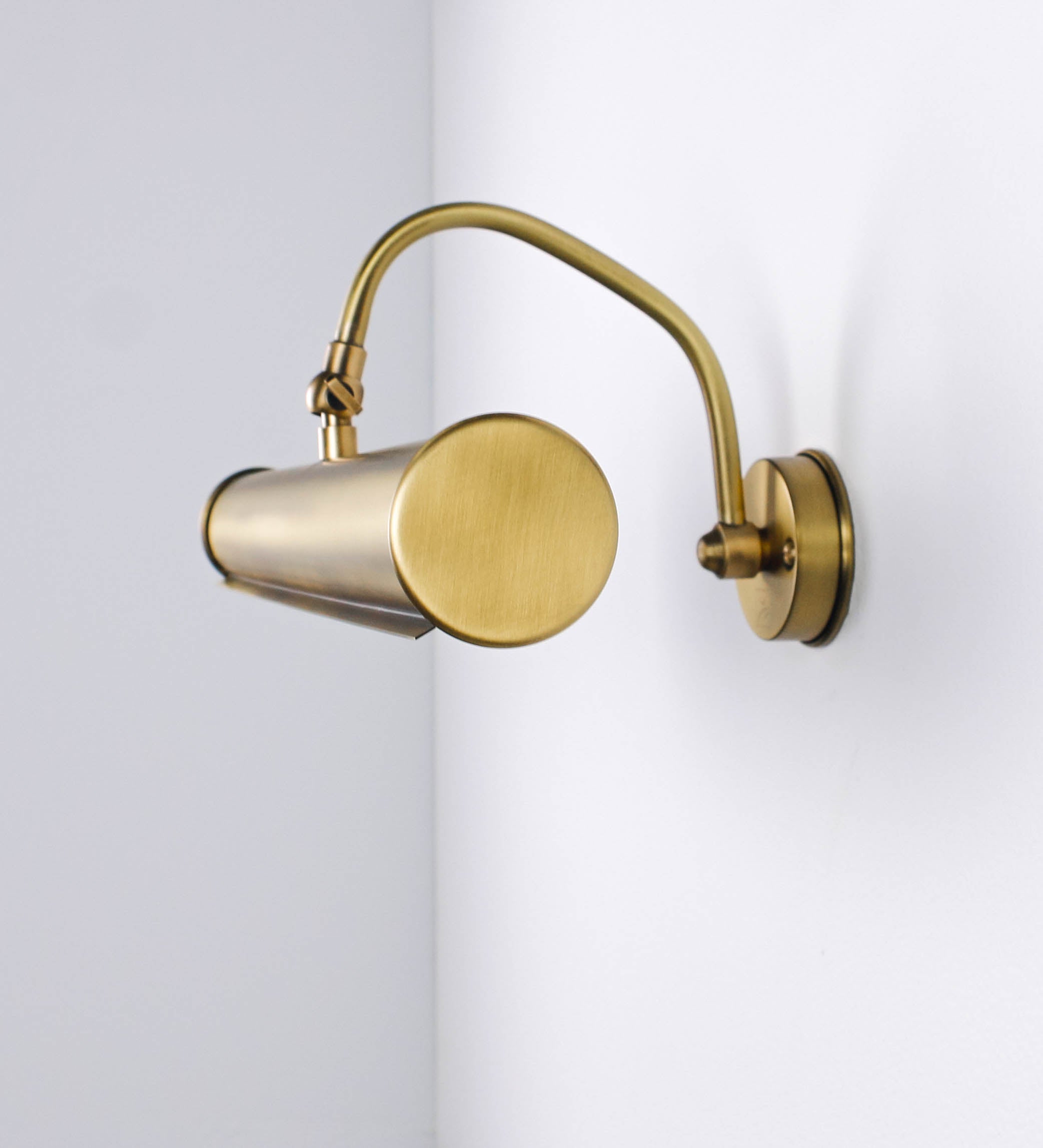 Aplique de parede que combina elementos clássicos com toques contemporâneos, todo em ouro velho. O aplique é composto por uma base circular de onde se estende um braço curvo e gracioso, que suporta a barra principal. O braço contém um elemento que permite apertar ou desapertar a barra para melhor manipular a direção da luz. A barra de 45cm de largura é cilíndrica e alongada. As extremidades do cilindro são planas e do mesmo diâmetro.