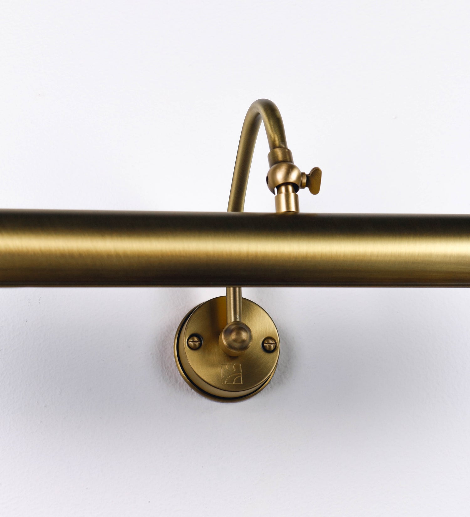 Aplique de parede que combina elementos clássicos com toques contemporâneos, todo em ouro velho. O aplique é composto por uma base circular de onde se estende um braço curvo e gracioso, que suporta a barra principal. O braço contém um elemento que permite apertar ou desapertar a barra para melhor manipular a direção da luz. A barra de 45cm de largura é cilíndrica e alongada. As extremidades do cilindro são planas e do mesmo diâmetro.