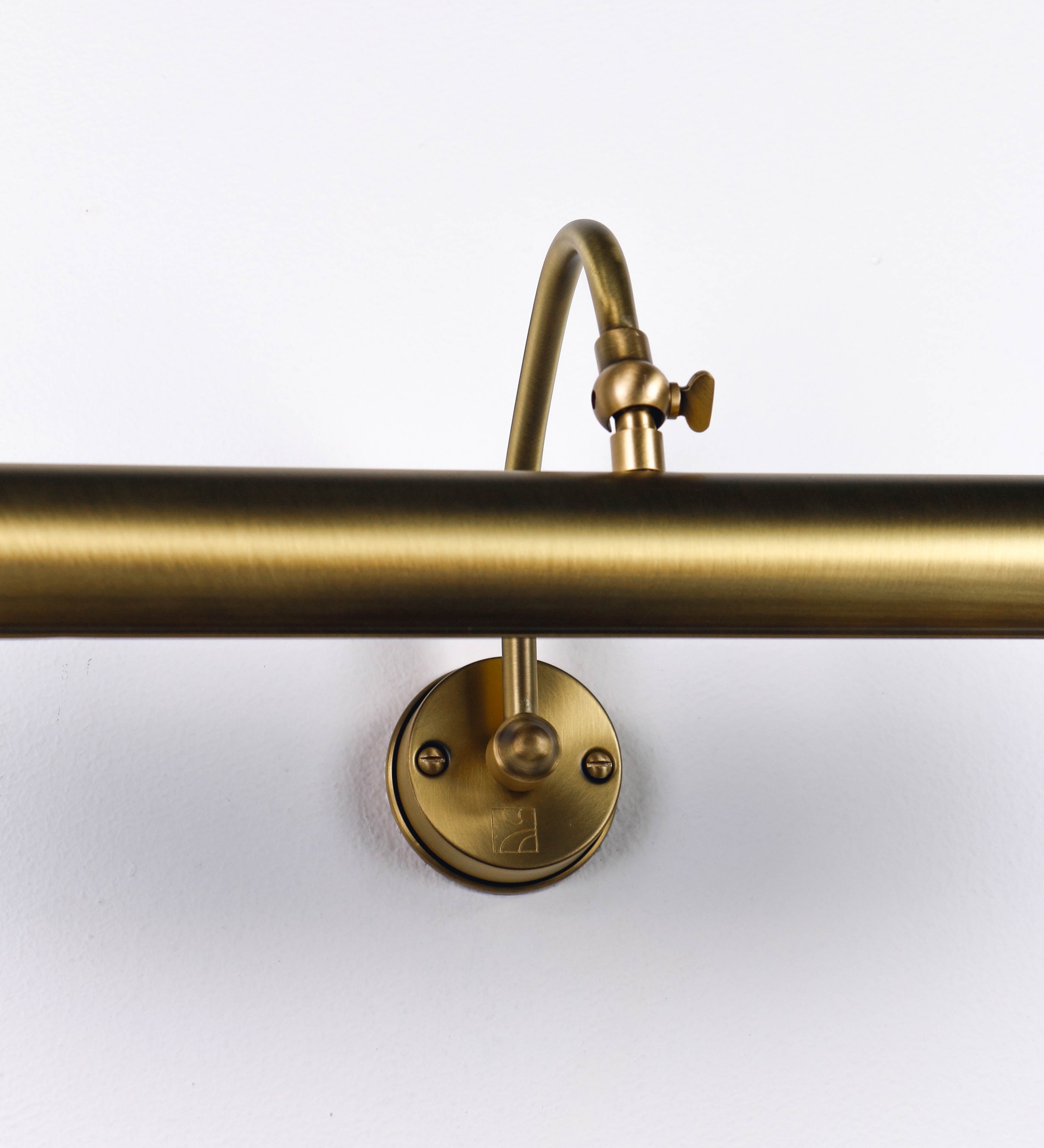 Aplique de parede que combina elementos clássicos com toques contemporâneos, todo em ouro velho. O aplique é composto por uma base circular de onde se estende um braço curvo e gracioso, que suporta a barra principal. O braço contém um elemento que permite apertar ou desapertar a barra para melhor manipular a direção da luz. A barra de 45cm de largura é cilíndrica e alongada. As extremidades do cilindro são planas e do mesmo diâmetro.