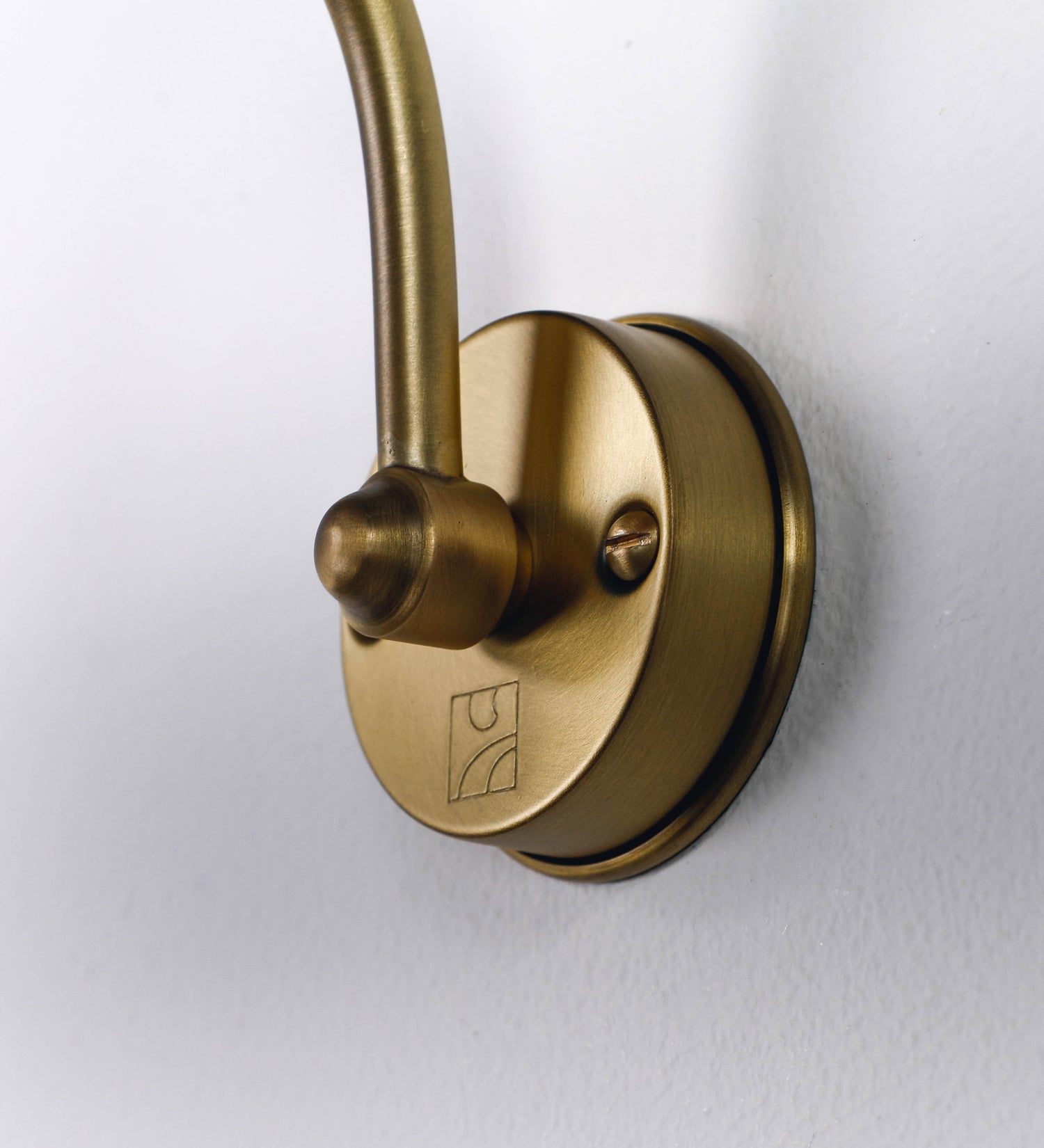 Aplique de parede que combina elementos clássicos com toques contemporâneos, todo em ouro velho. O aplique é composto por uma base circular de onde se estende um braço curvo e gracioso, que suporta a barra principal. O braço contém um elemento que permite apertar ou desapertar a barra para melhor manipular a direção da luz. A barra de 45cm de largura é cilíndrica e alongada. As extremidades do cilindro são planas e do mesmo diâmetro.