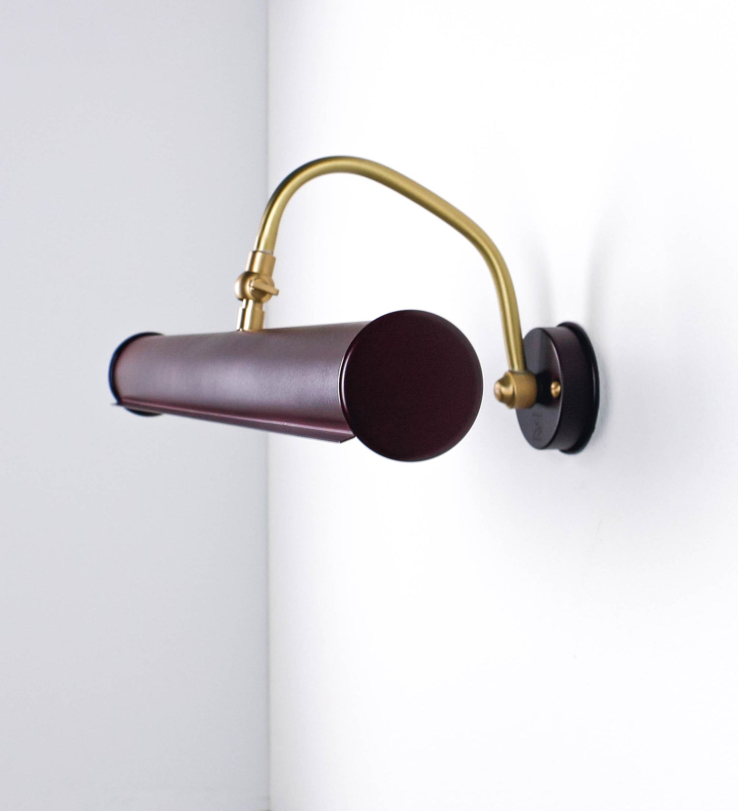 Aplique de parede que combina elementos clássicos com toques contemporâneos. O aplique é composto por uma base circular tom vinho, de onde se estende um braço curvo e gracioso, em latão escovado, que suporta a barra principal. O braço contém um elemento, em latão escovado, que permite apertar ou desapertar a barra para melhor manipular a direção da luz. A barra de 45cm de largura, é cilíndrica e alongada, tom vinho. As extremidades do cilindro são planas e do mesmo diâmetro.