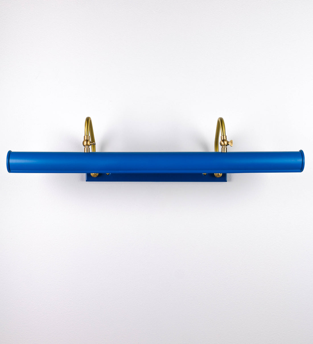 Aplique de parede que combina elementos clássicos com toques contemporâneos. O aplique é composto por uma base retangular azul vintage, de onde se estendem dois braços curvos e graciosos, em latão escovado, que suportam a barra principal. Os braços contêm um elemento, em latão escovado, que permite apertar ou desapertar a barra para melhor manipular a direção da luz. A barra de 65cm de largura, é cilíndrica e alongada, azul vintage. As extremidades do cilindro são planas e do mesmo diâmetro.