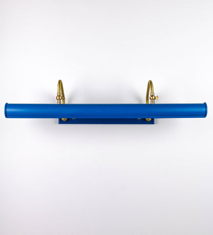 Aplique de parede que combina elementos clássicos com toques contemporâneos. O aplique é composto por uma base retangular azul vintage, de onde se estendem dois braços curvos e graciosos, em latão escovado, que suportam a barra principal. Os braços contêm um elemento, em latão escovado, que permite apertar ou desapertar a barra para melhor manipular a direção da luz. A barra de 65cm de largura, é cilíndrica e alongada, azul vintage. As extremidades do cilindro são planas e do mesmo diâmetro.
