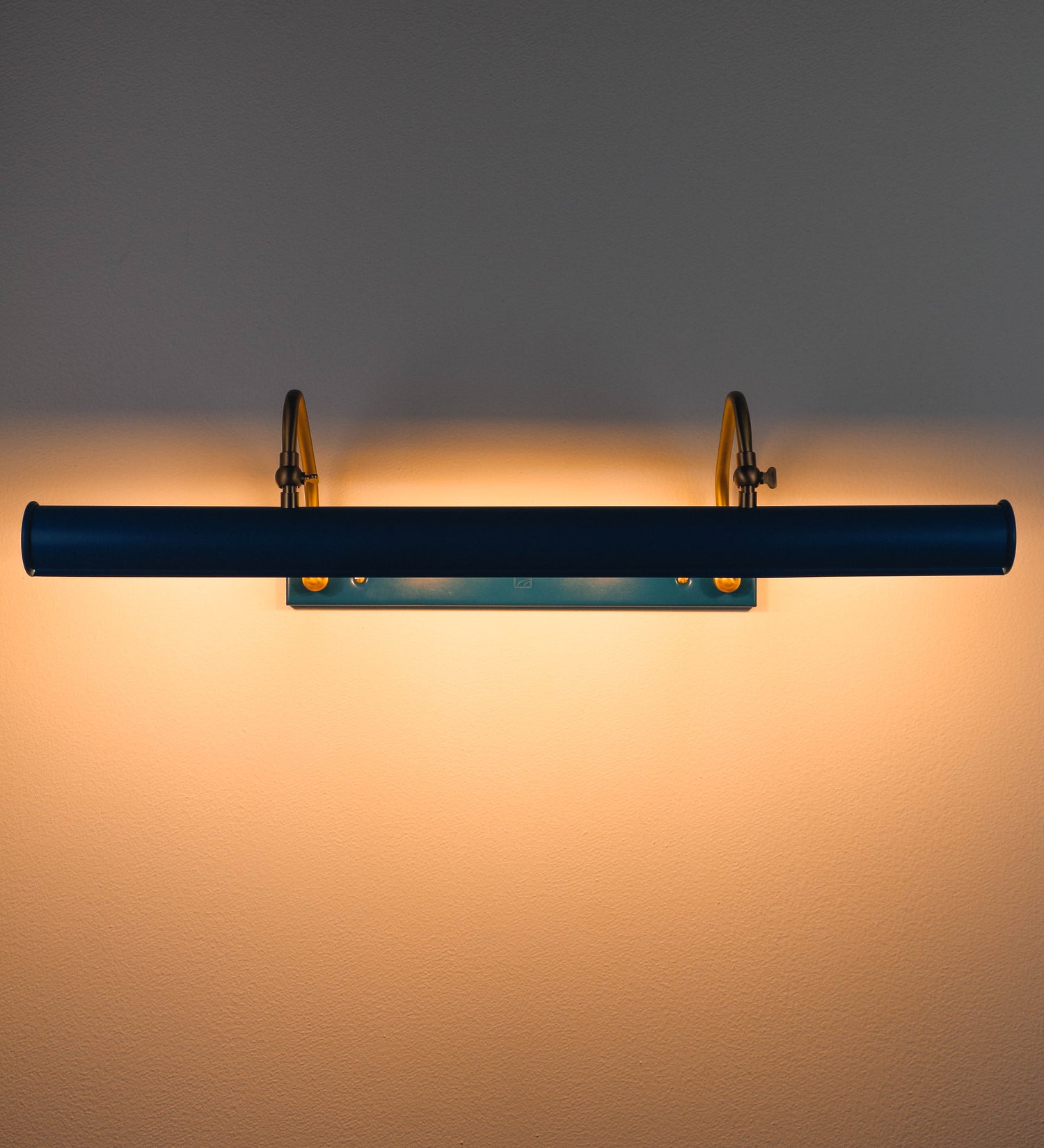 Aplique de parede que combina elementos clássicos com toques contemporâneos. O aplique é composto por uma base retangular azul vintage, de onde se estendem dois braços curvos e graciosos, em latão escovado, que suportam a barra principal. Os braços contêm um elemento, em latão escovado, que permite apertar ou desapertar a barra para melhor manipular a direção da luz. A barra de 65cm de largura, é cilíndrica e alongada, azul vintage. As extremidades do cilindro são planas e do mesmo diâmetro.