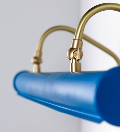 Aplique de parede que combina elementos clássicos com toques contemporâneos. O aplique é composto por uma base retangular azul vintage, de onde se estendem dois braços curvos e graciosos, em latão escovado, que suportam a barra principal. Os braços contêm um elemento, em latão escovado, que permite apertar ou desapertar a barra para melhor manipular a direção da luz. A barra de 65cm de largura, é cilíndrica e alongada, azul vintage. As extremidades do cilindro são planas e do mesmo diâmetro.