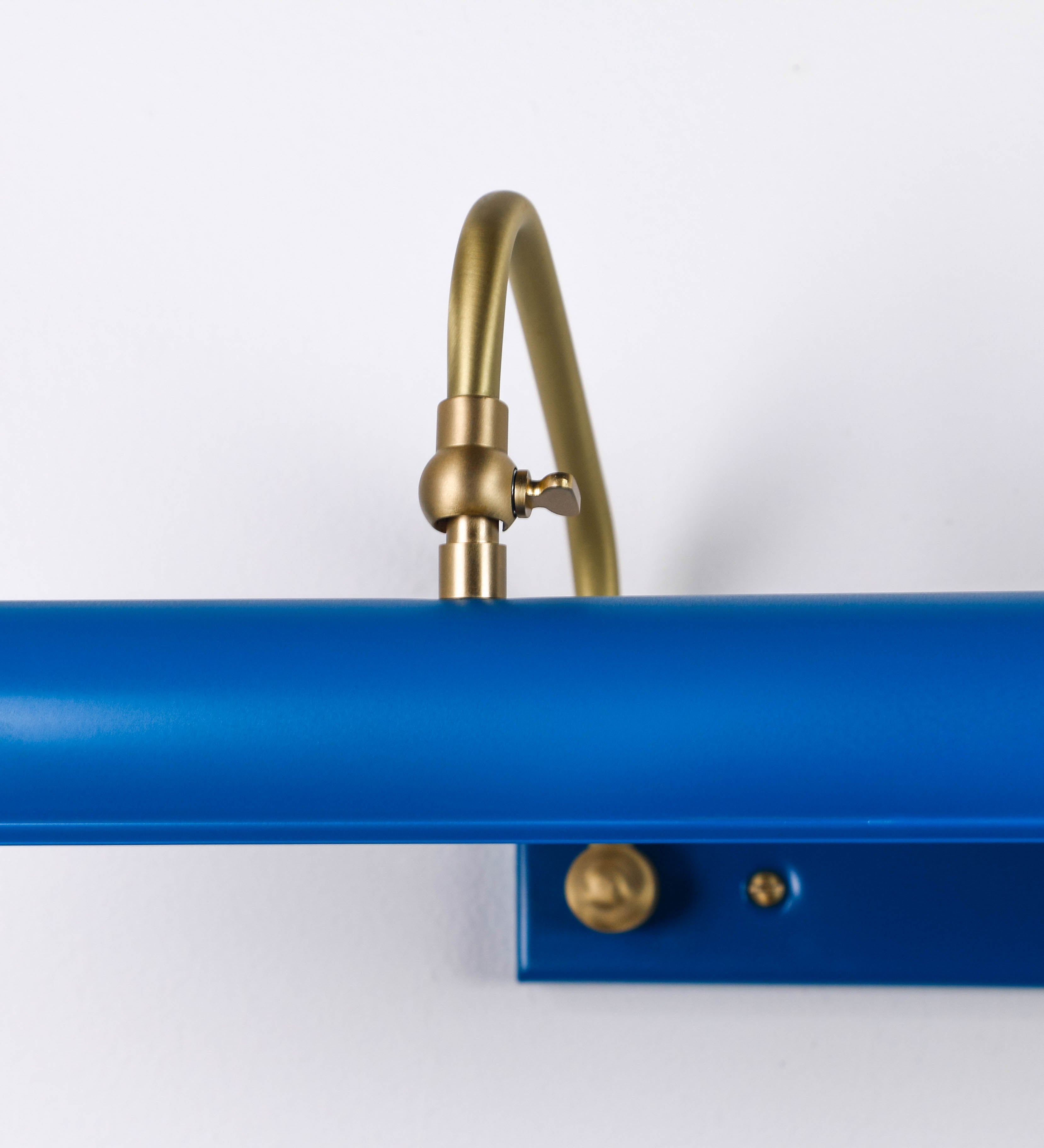 Aplique de parede que combina elementos clássicos com toques contemporâneos. O aplique é composto por uma base retangular azul vintage, de onde se estendem dois braços curvos e graciosos, em latão escovado, que suportam a barra principal. Os braços contêm um elemento, em latão escovado, que permite apertar ou desapertar a barra para melhor manipular a direção da luz. A barra de 65cm de largura, é cilíndrica e alongada, azul vintage. As extremidades do cilindro são planas e do mesmo diâmetro.