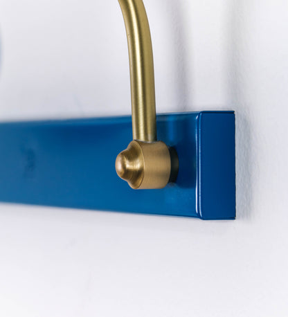 Aplique de parede que combina elementos clássicos com toques contemporâneos. O aplique é composto por uma base retangular azul vintage, de onde se estendem dois braços curvos e graciosos, em latão escovado, que suportam a barra principal. Os braços contêm um elemento, em latão escovado, que permite apertar ou desapertar a barra para melhor manipular a direção da luz. A barra de 65cm de largura, é cilíndrica e alongada, azul vintage. As extremidades do cilindro são planas e do mesmo diâmetro.
