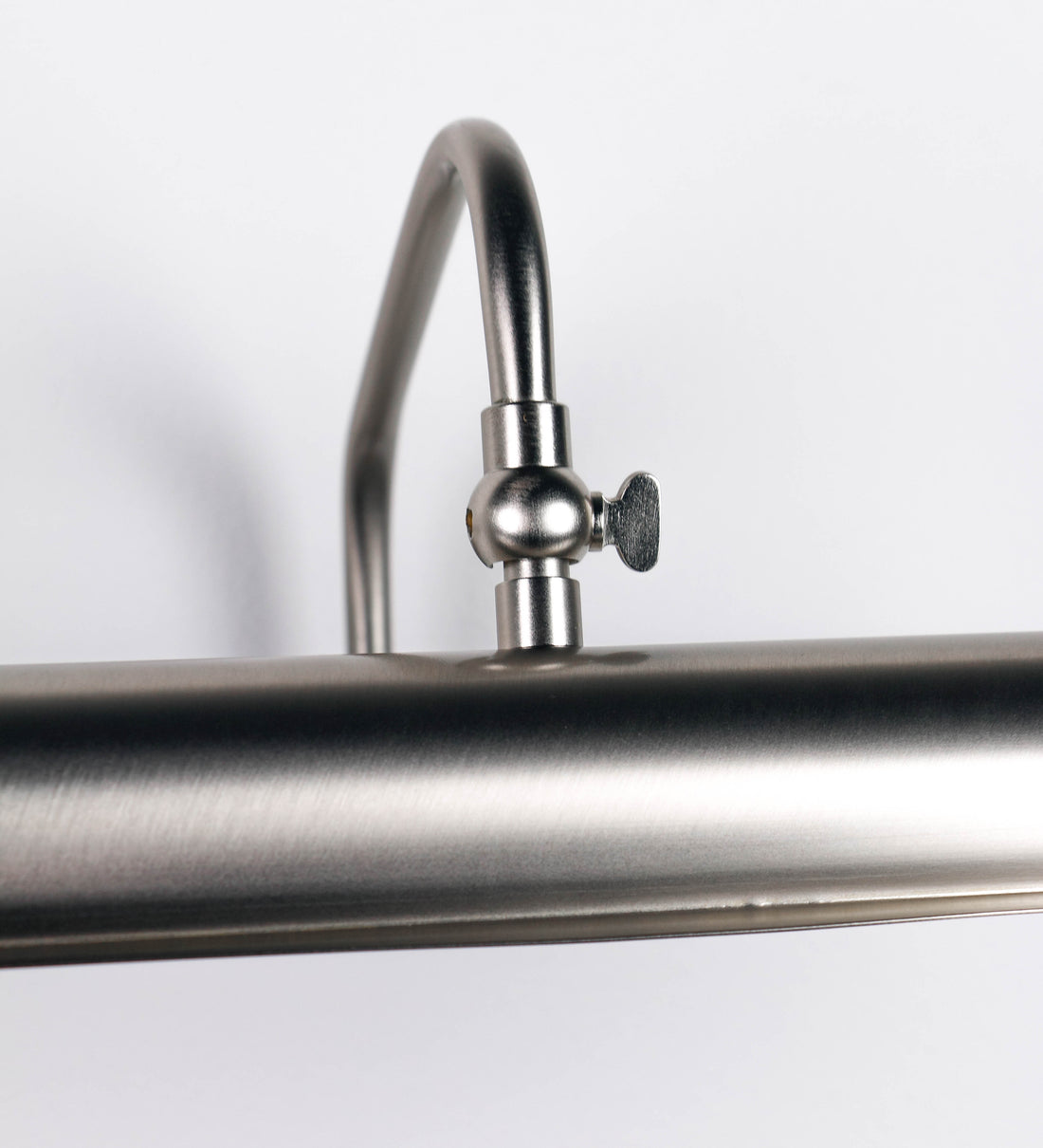 Aplique de parede que combina elementos clássicos com toques contemporâneos, todo em níquel escovado. O aplique é composto por uma base retangular, de onde se estendem dois braços curvos e graciosos, que suportam a barra principal. Os braços contêm um elemento que permite apertar ou desapertar a barra para melhor manipular a direção da luz. A barra de 65cm de largura é cilíndrica e alongada. As extremidades do cilindro são planas e do mesmo diâmetro.