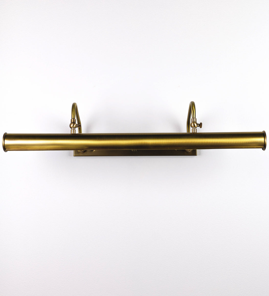Aplique de parede que combina elementos clássicos com toques contemporâneos, todo em ouro velho. O aplique é composto por uma base retangular, de onde se estendem dois braços curvos e graciosos, que suportam a barra principal. Os braços contêm um elemento que permite apertar ou desapertar a barra para melhor manipular a direção da luz. A barra de 65cm de largura é cilíndrica e alongada. As extremidades do cilindro são planas e do mesmo diâmetro.