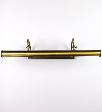 Aplique de parede que combina elementos clássicos com toques contemporâneos, todo em ouro velho. O aplique é composto por uma base retangular, de onde se estendem dois braços curvos e graciosos, que suportam a barra principal. Os braços contêm um elemento que permite apertar ou desapertar a barra para melhor manipular a direção da luz. A barra de 65cm de largura é cilíndrica e alongada. As extremidades do cilindro são planas e do mesmo diâmetro.