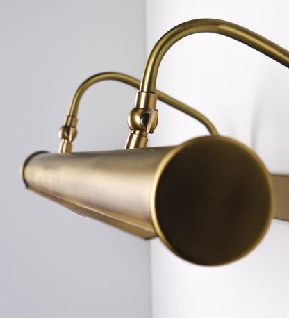 Aplique de parede que combina elementos clássicos com toques contemporâneos, todo em ouro velho. O aplique é composto por uma base retangular, de onde se estendem dois braços curvos e graciosos, que suportam a barra principal. Os braços contêm um elemento que permite apertar ou desapertar a barra para melhor manipular a direção da luz. A barra de 65cm de largura é cilíndrica e alongada. As extremidades do cilindro são planas e do mesmo diâmetro.