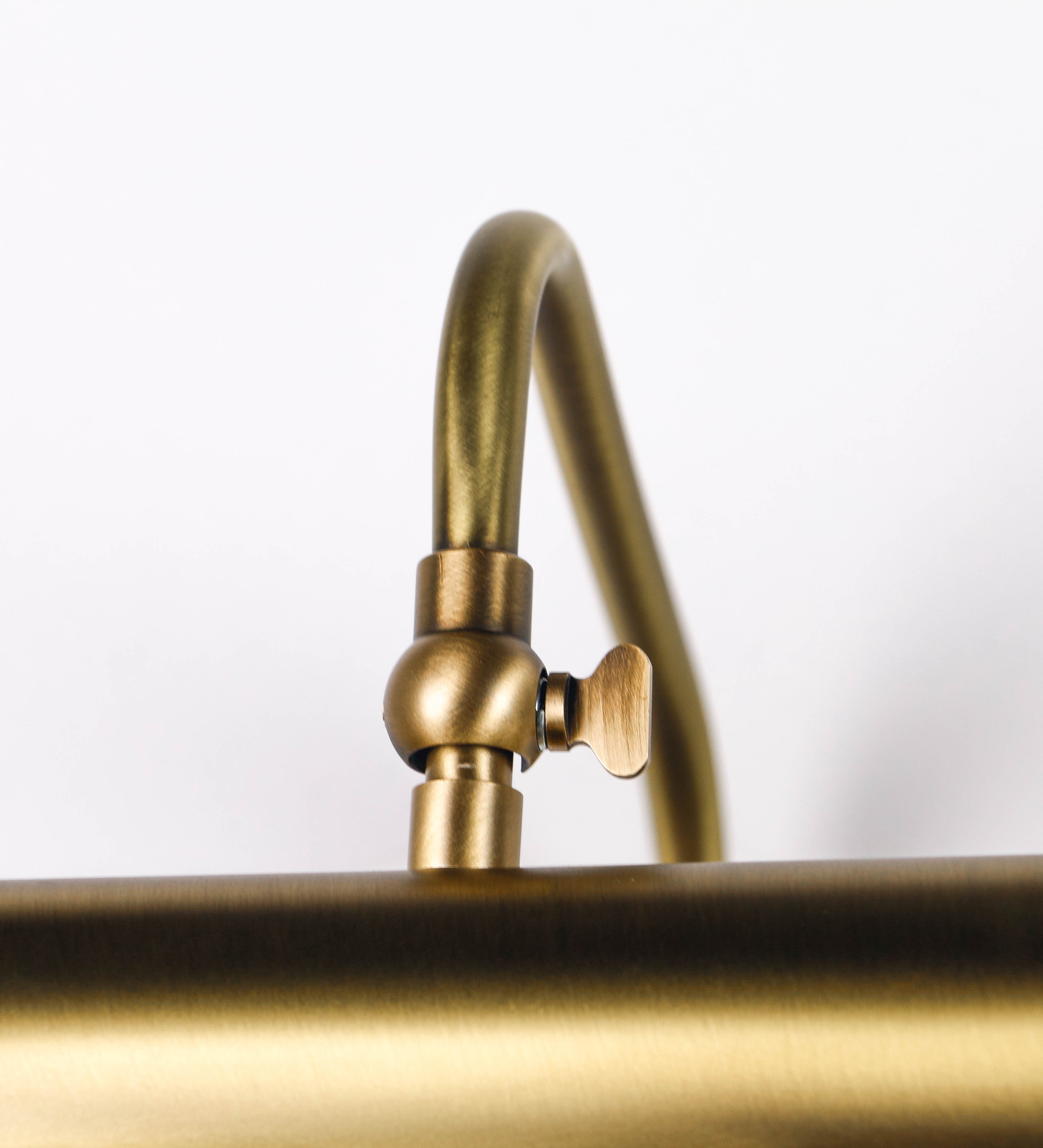 Aplique de parede que combina elementos clássicos com toques contemporâneos, todo em ouro velho. O aplique é composto por uma base retangular, de onde se estendem dois braços curvos e graciosos, que suportam a barra principal. Os braços contêm um elemento que permite apertar ou desapertar a barra para melhor manipular a direção da luz. A barra de 65cm de largura é cilíndrica e alongada. As extremidades do cilindro são planas e do mesmo diâmetro.