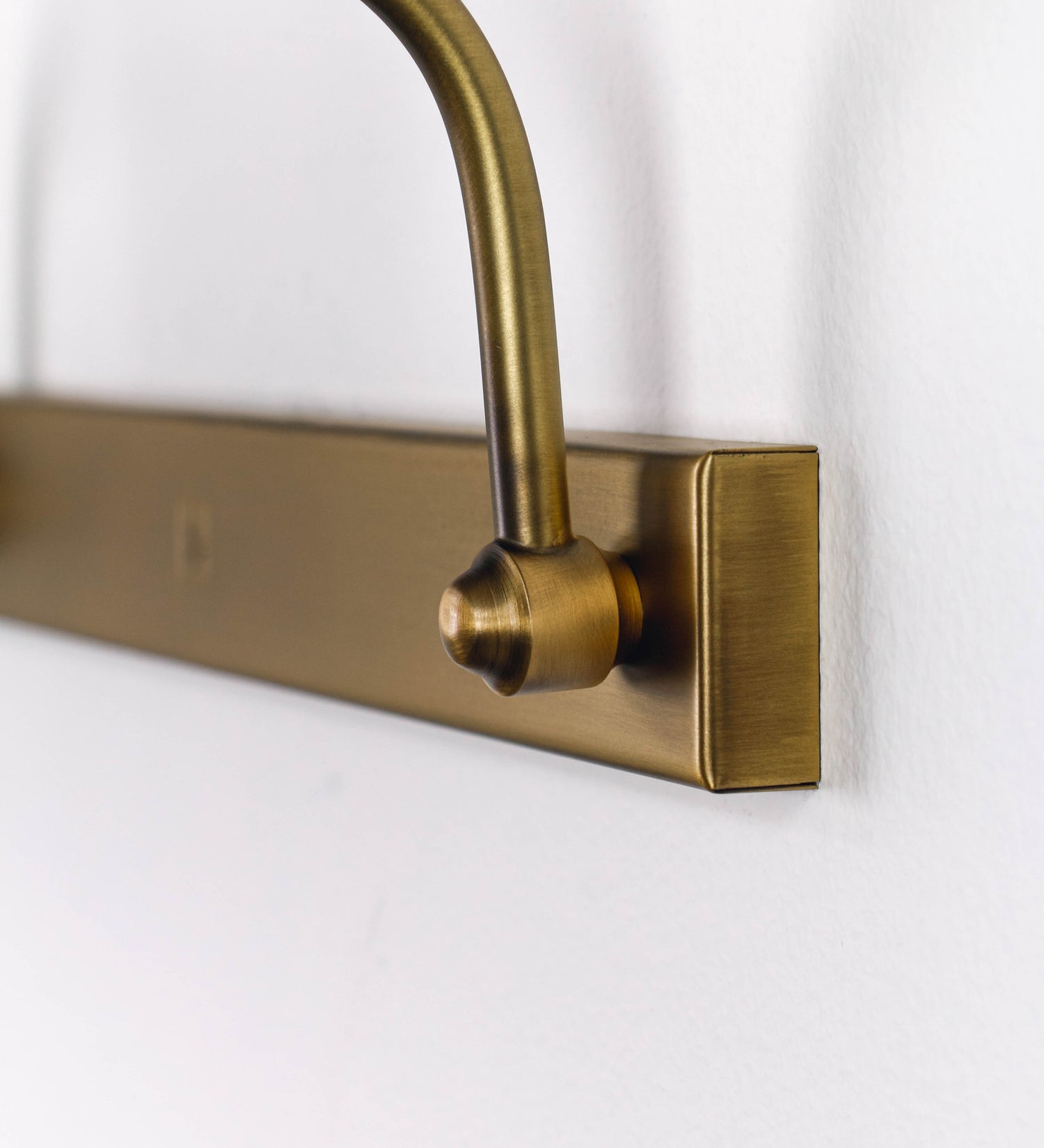 Aplique de parede que combina elementos clássicos com toques contemporâneos, todo em ouro velho. O aplique é composto por uma base retangular, de onde se estendem dois braços curvos e graciosos, que suportam a barra principal. Os braços contêm um elemento que permite apertar ou desapertar a barra para melhor manipular a direção da luz. A barra de 65cm de largura é cilíndrica e alongada. As extremidades do cilindro são planas e do mesmo diâmetro.