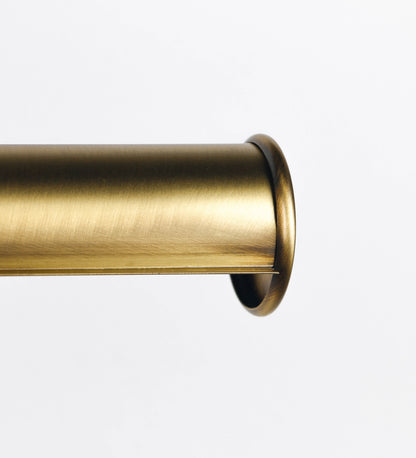 Aplique de parede que combina elementos clássicos com toques contemporâneos, todo em ouro velho. O aplique é composto por uma base retangular, de onde se estendem dois braços curvos e graciosos, que suportam a barra principal. Os braços contêm um elemento que permite apertar ou desapertar a barra para melhor manipular a direção da luz. A barra de 65cm de largura é cilíndrica e alongada. As extremidades do cilindro são planas e do mesmo diâmetro.