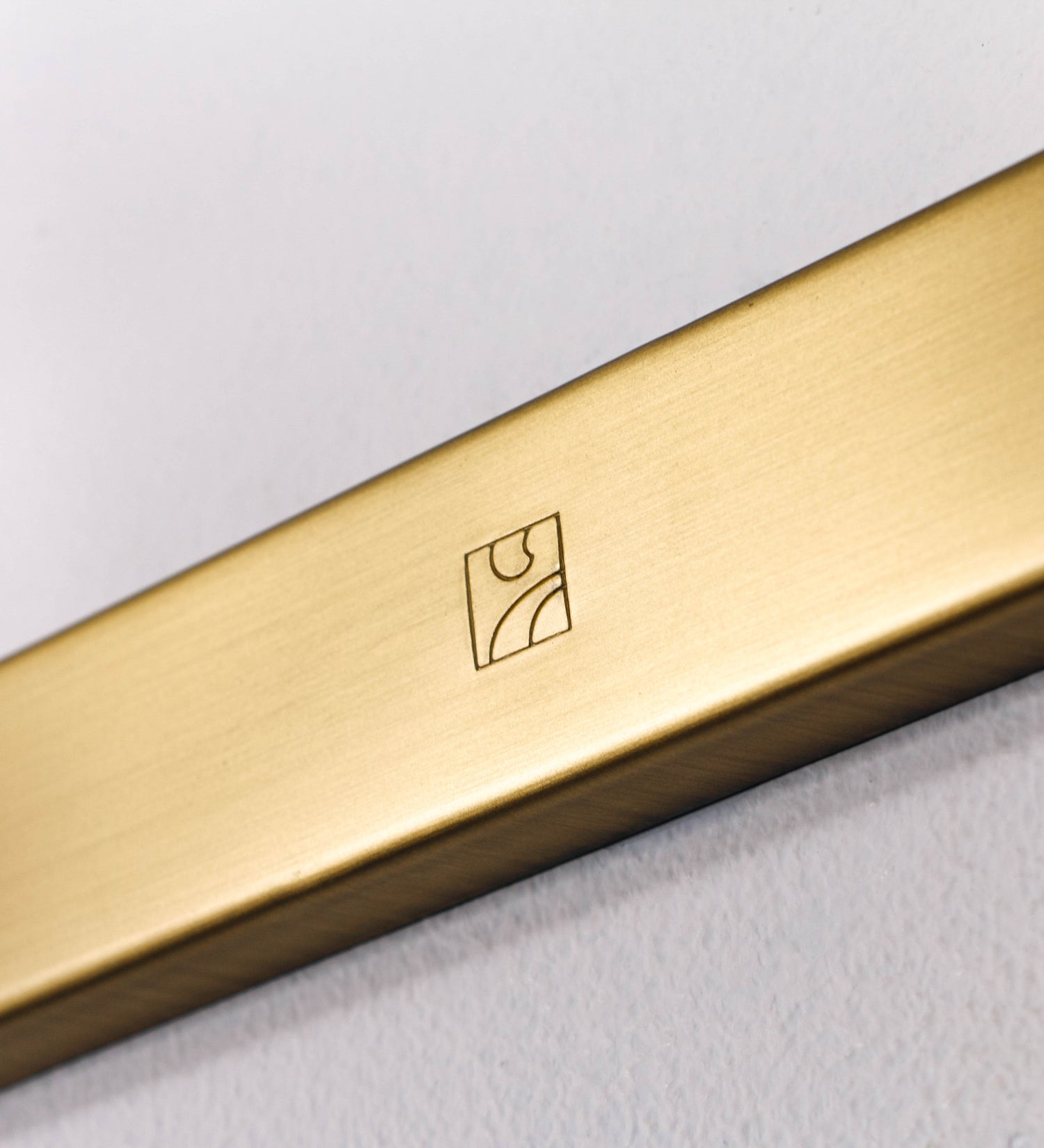 Aplique de parede que combina elementos clássicos com toques contemporâneos, todo em ouro velho. O aplique é composto por uma base retangular, de onde se estendem dois braços curvos e graciosos, que suportam a barra principal. Os braços contêm um elemento que permite apertar ou desapertar a barra para melhor manipular a direção da luz. A barra de 65cm de largura é cilíndrica e alongada. As extremidades do cilindro são planas e do mesmo diâmetro.