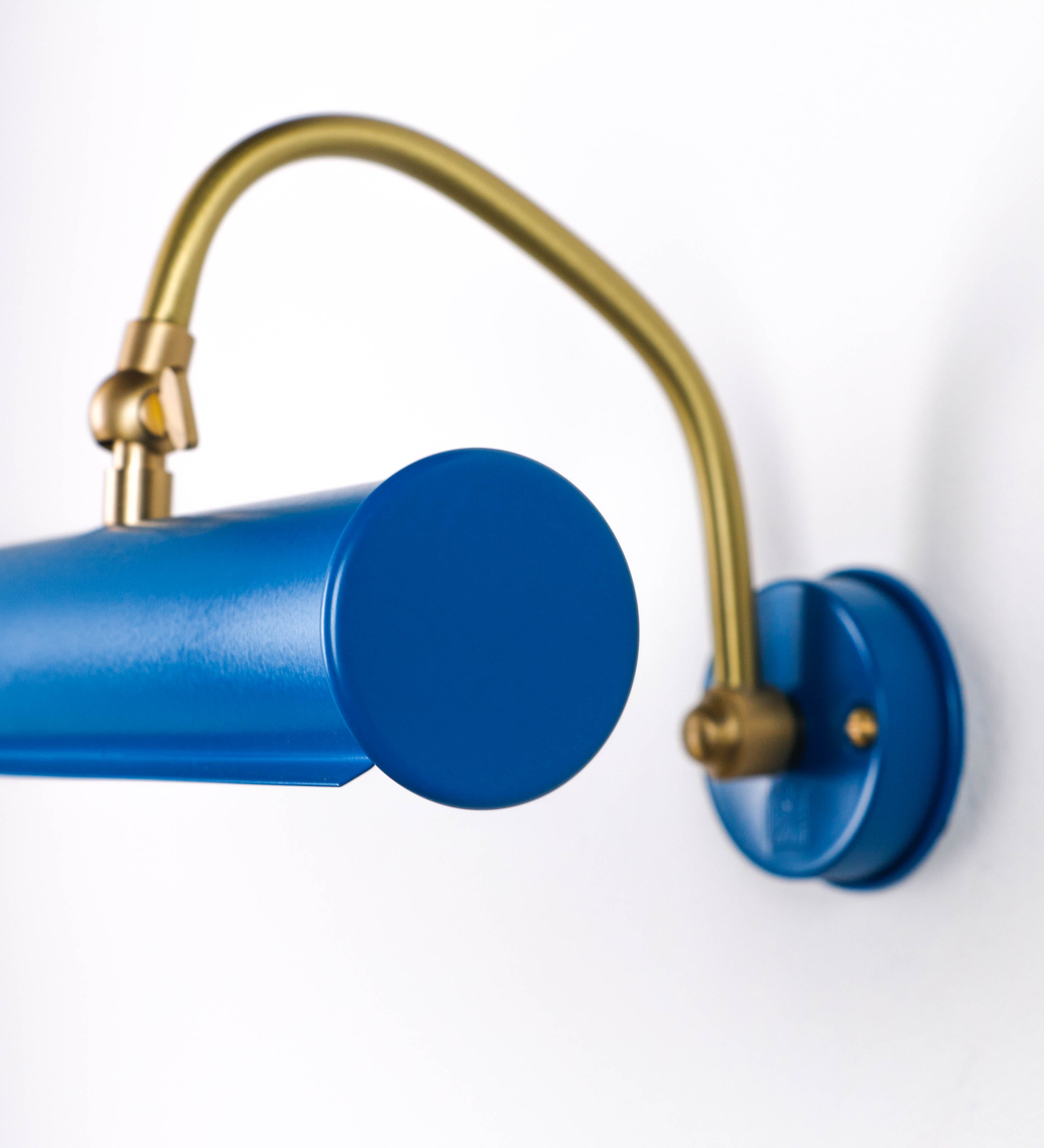 Aplique de parede que combina elementos clássicos com toques contemporâneos. O aplique é composto por uma base circular azul vintage de onde se estende um braço curvo e gracioso, em latão escovado, que suporta a barra principal. O braço contém um elemento, em latão escovado, que permite apertar ou desapertar a barra para melhor manipular a direção da luz. A barra de 25cm de largura, é cilíndrica e alongada, azul vintage. As extremidades do cilindro são planas e do mesmo diâmetro.