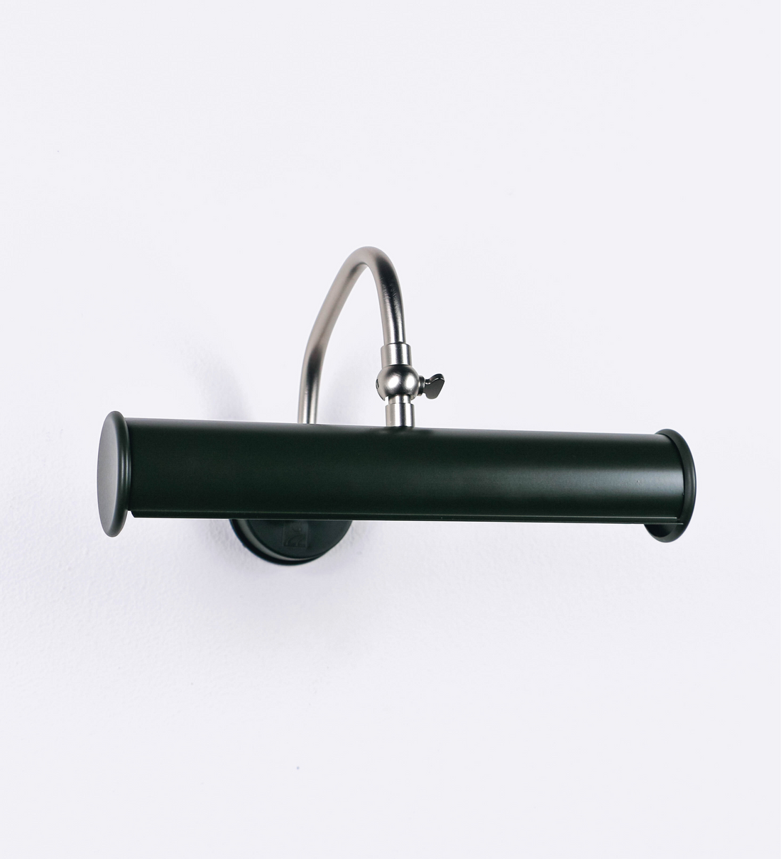 Aplique de parede que combina elementos clássicos com toques contemporâneos. O aplique é composto por uma base circular verde-azeitona, de onde se estende um braço curvo e gracioso, em níquel escovado, que suporta a barra principal. O braço contém um elemento, em níquel escovado, que permite apertar ou desapertar a barra para melhor manipular a direção da luz. A barra de 25cm de largura, é cilíndrica e alongada, verde-azeitona. As extremidades do cilindro são planas e do mesmo diâmetro.