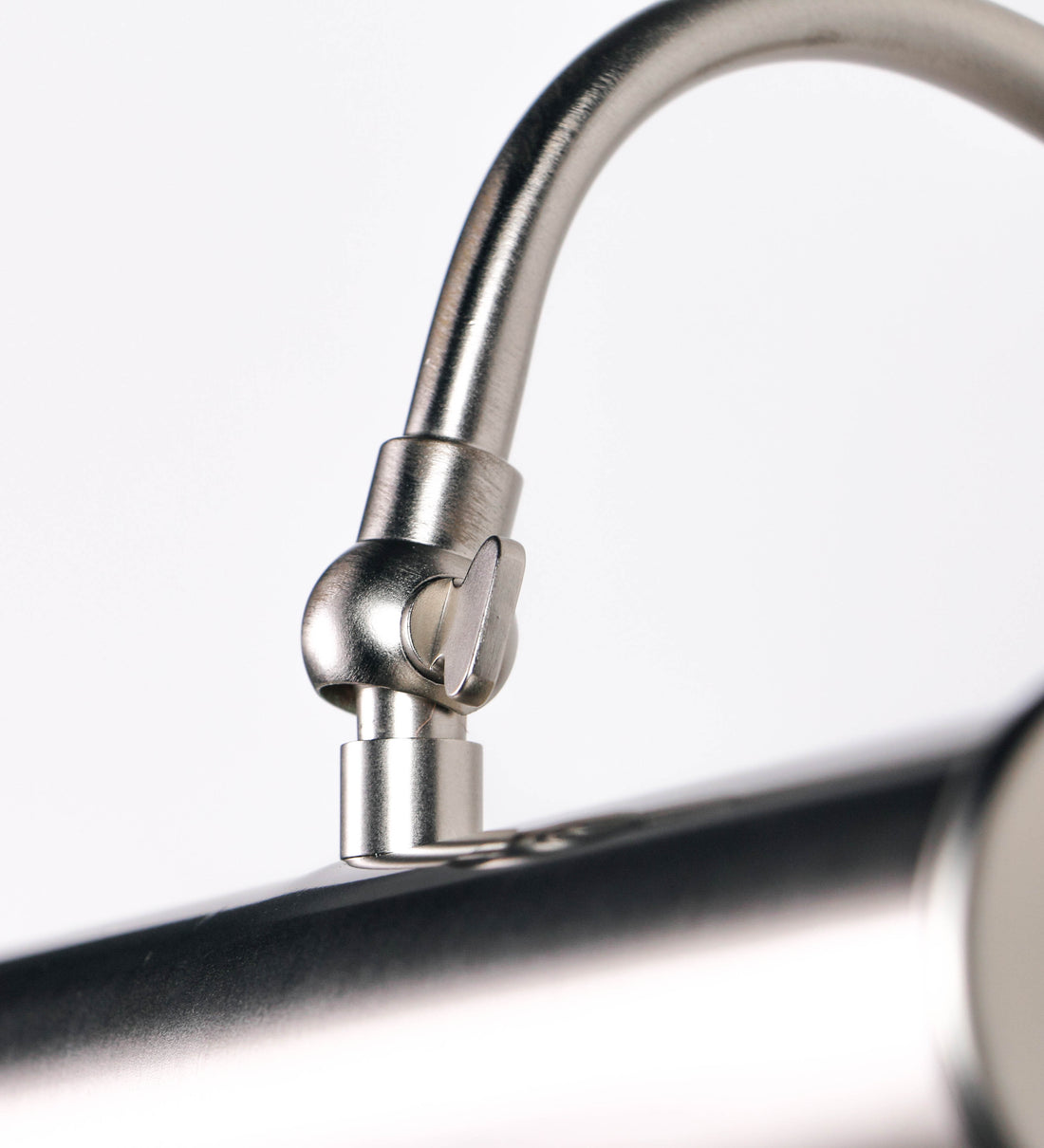 Aplique de parede que combina elementos clássicos com toques contemporâneos, todo em níquel escovado. O aplique é composto por uma base circular de onde se estende um braço curvo e gracioso, que suporta a barra principal. O braço contém um elemento que permite apertar ou desapertar a barra para melhor manipular a direção da luz. A barra de 25cm de largura é cilíndrica e alongada. As extremidades do cilindro são planas e do mesmo diâmetro.