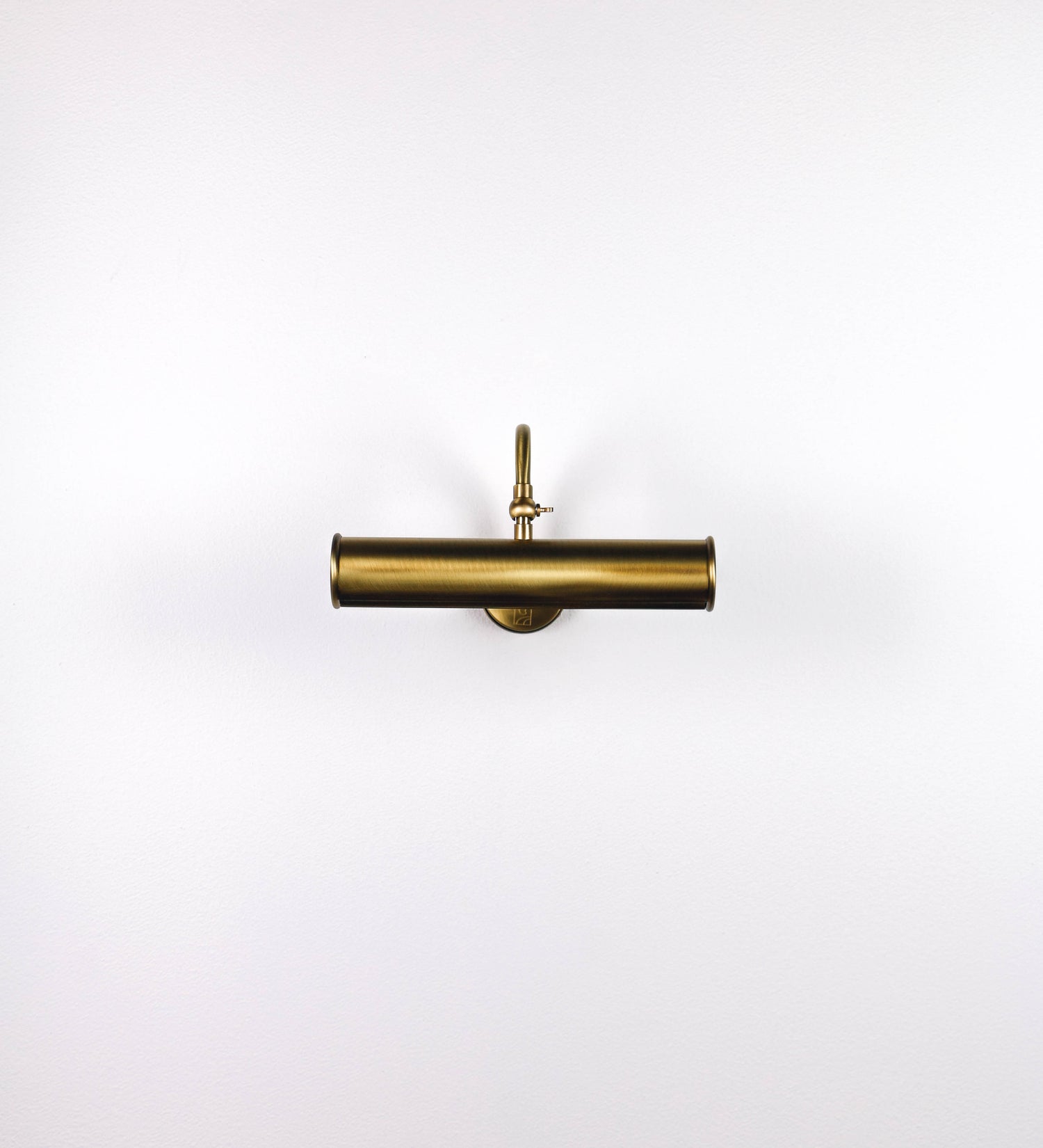 Aplique de parede que combina elementos clássicos com toques contemporâneos, todo em ouro velho. O aplique é composto por uma base circular de onde se estende um braço curvo e gracioso, que suporta a barra principal. O braço contém um elemento que permite apertar ou desapertar a barra para melhor manipular a direção da luz. A barra de 25cm de largura é cilíndrica e alongada. As extremidades do cilindro são planas e do mesmo diâmetro.