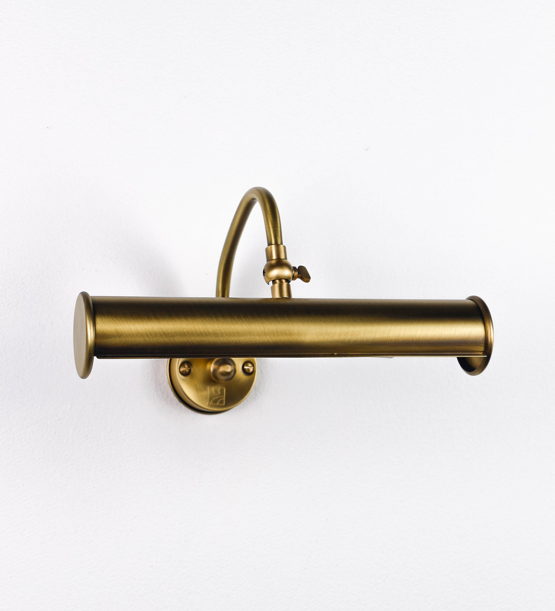 Aplique de parede que combina elementos clássicos com toques contemporâneos, todo em ouro velho. O aplique é composto por uma base circular de onde se estende um braço curvo e gracioso, que suporta a barra principal. O braço contém um elemento que permite apertar ou desapertar a barra para melhor manipular a direção da luz. A barra de 25cm de largura é cilíndrica e alongada. As extremidades do cilindro são planas e do mesmo diâmetro.